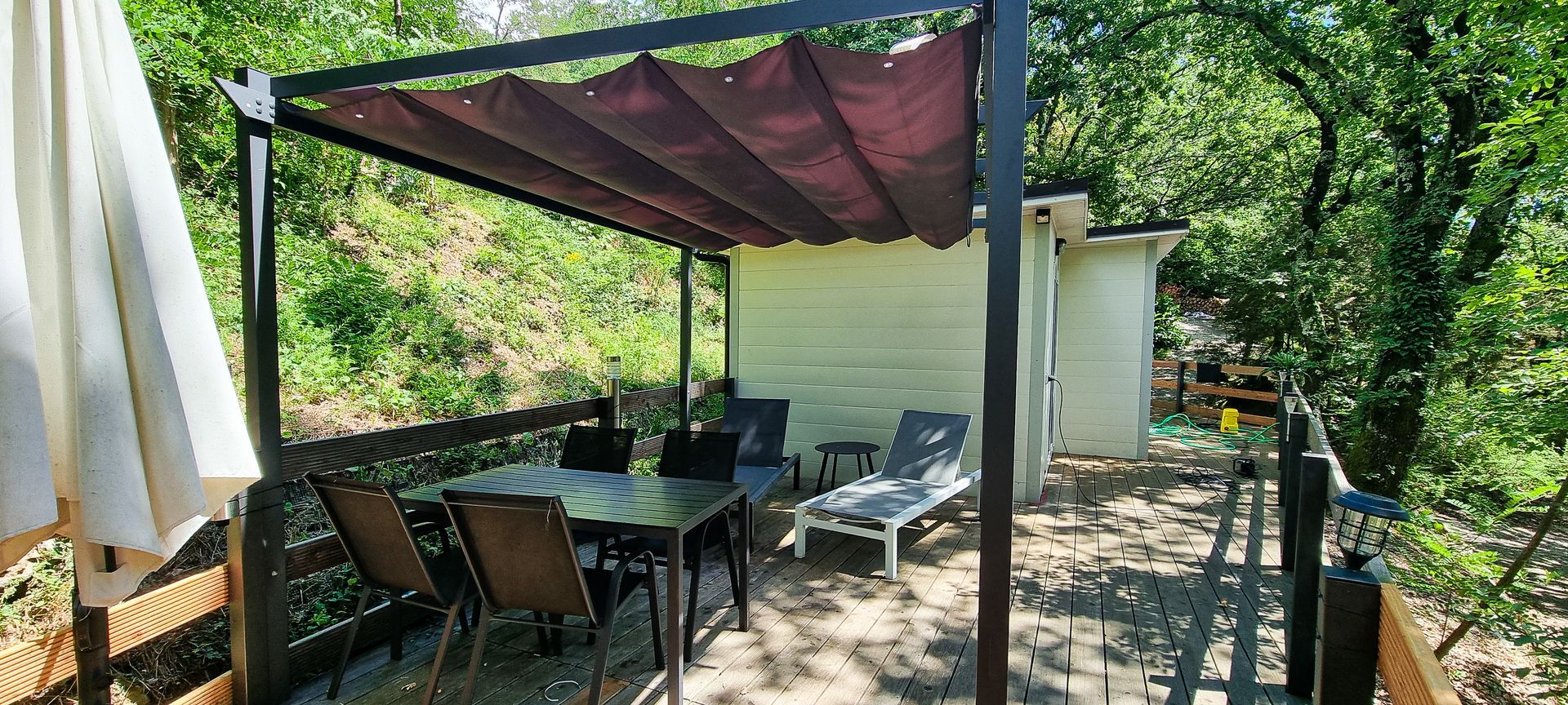 Buitenpatio met een tafel, stoelen en 2 ligstoelen. Omgeven door bomen.