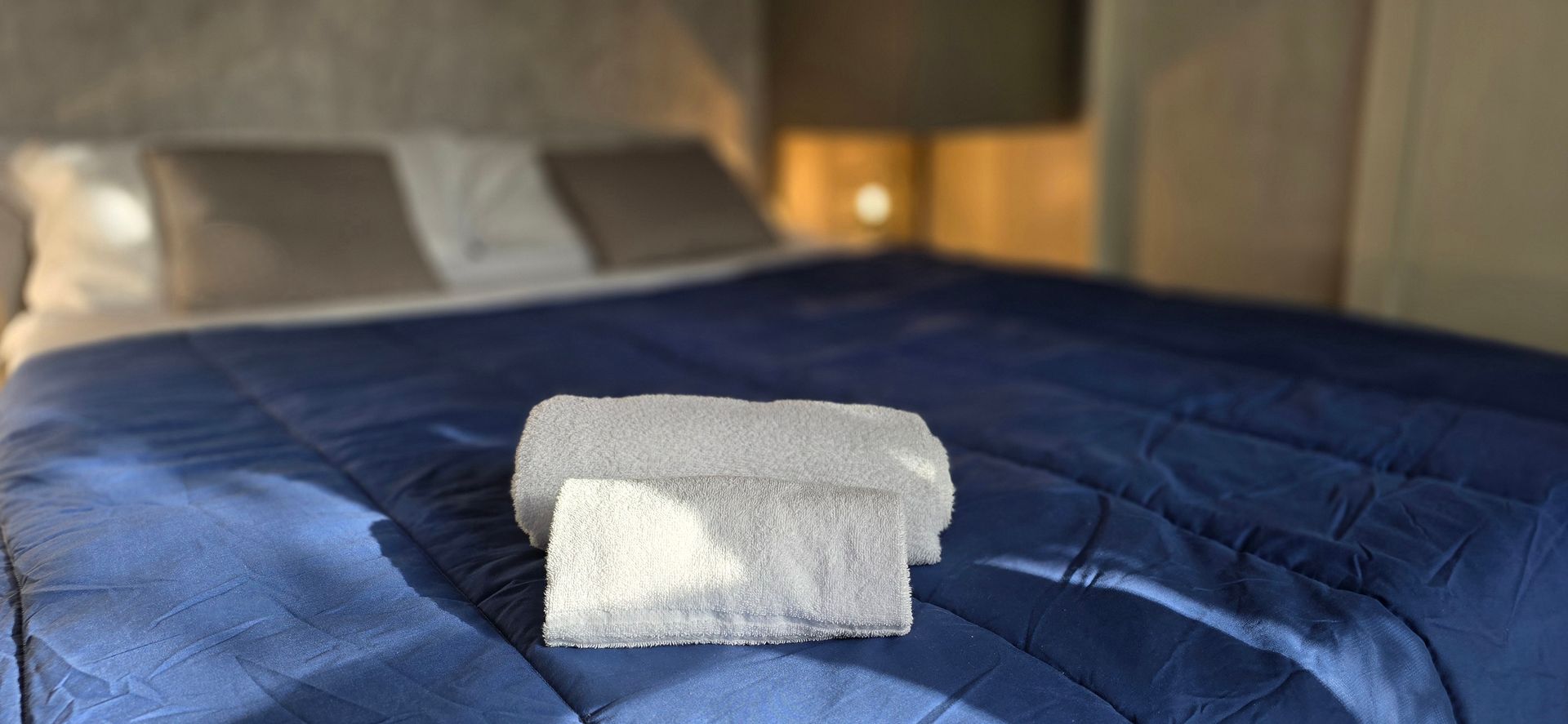 Een bed met een blauw dekbed, witte handdoeken en kussens. Een nachtlampje is zichtbaar.