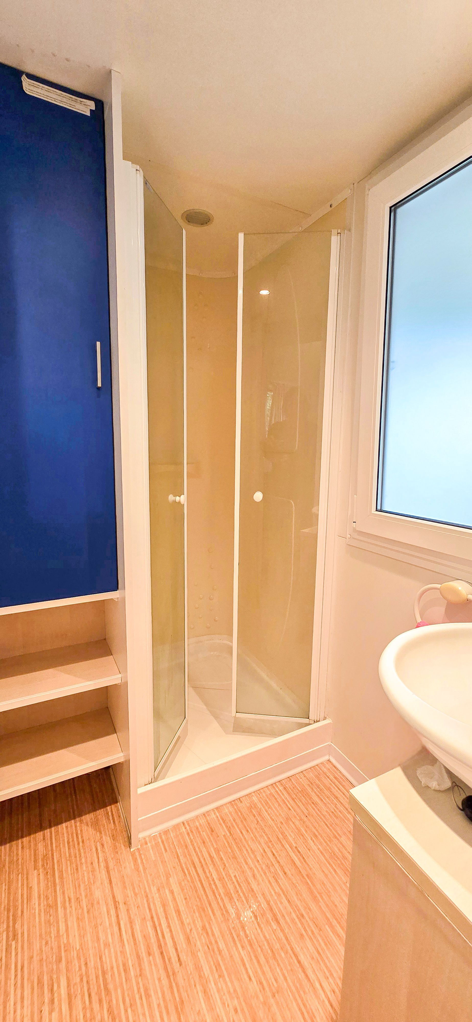 Kleine badkamer met een douche, wastafel en blauw kastje.