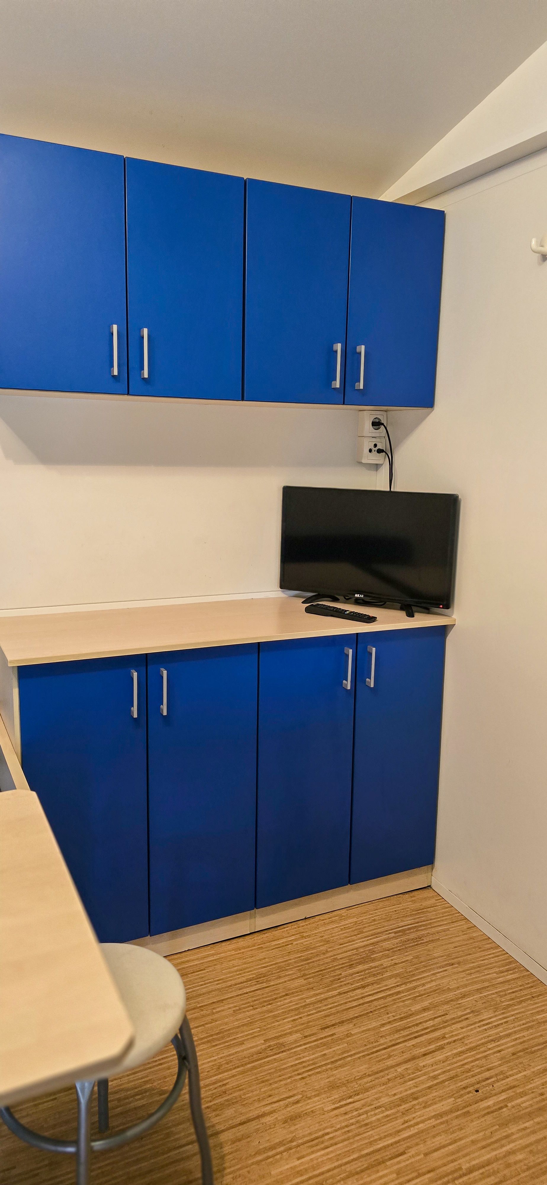 Blauwe kasten en een tv in een kleine kamer met een beige vloerkleed en een tafel.