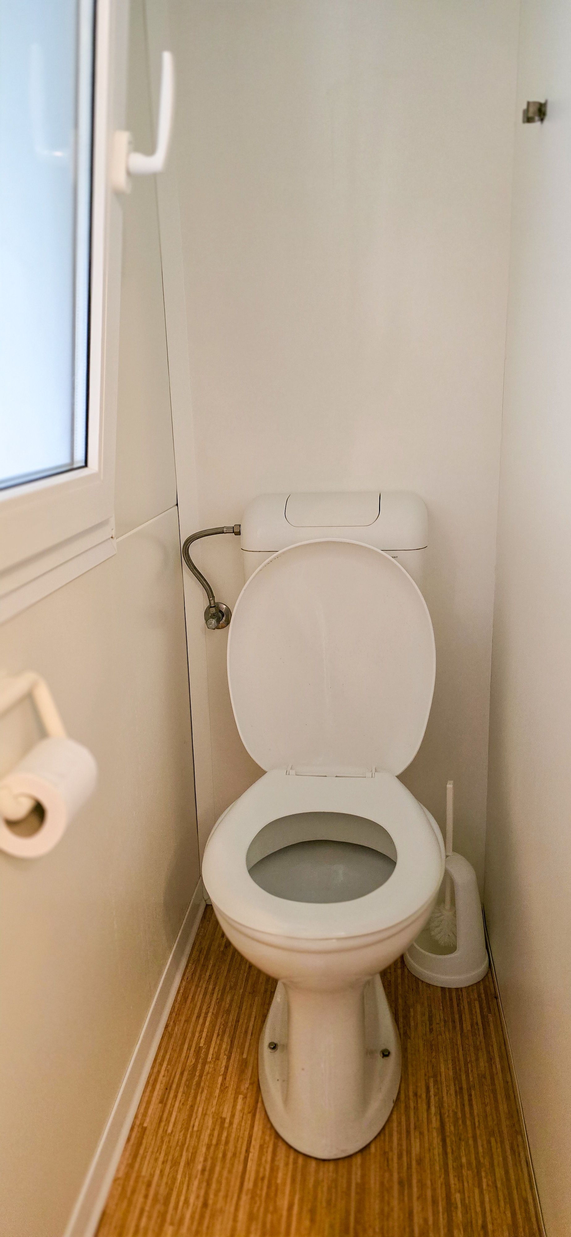 Wit toilet met houten vloer en een raam.