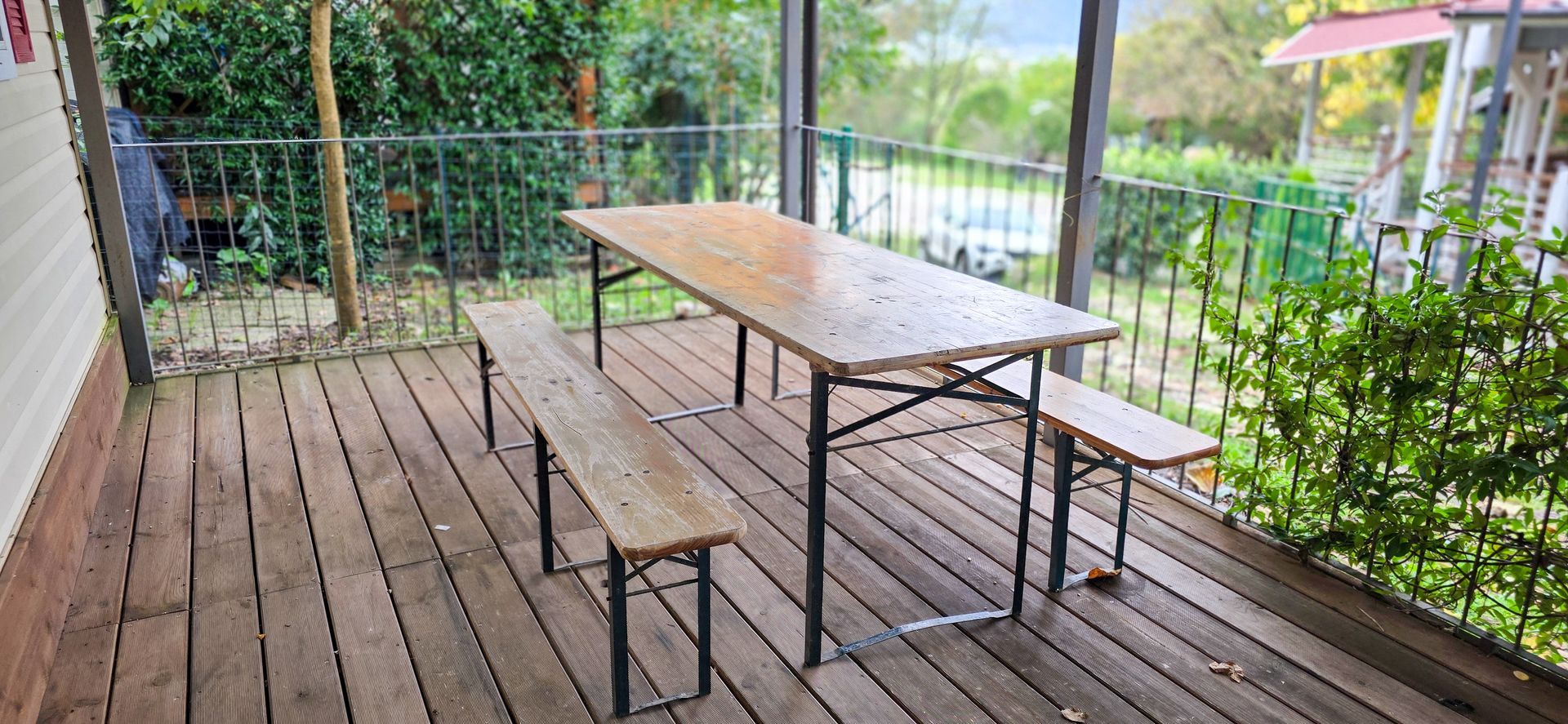 Houten tafel en banken op het terras, met een metalen reling, met uitzicht op het groen.