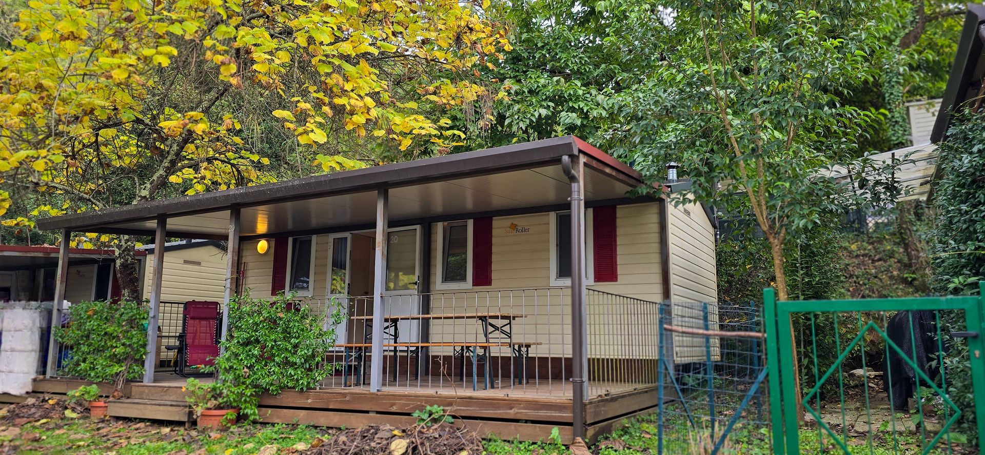 Chalet met een veranda, beige muren en rode luiken. De blokhut is omgeven door groene bomen.