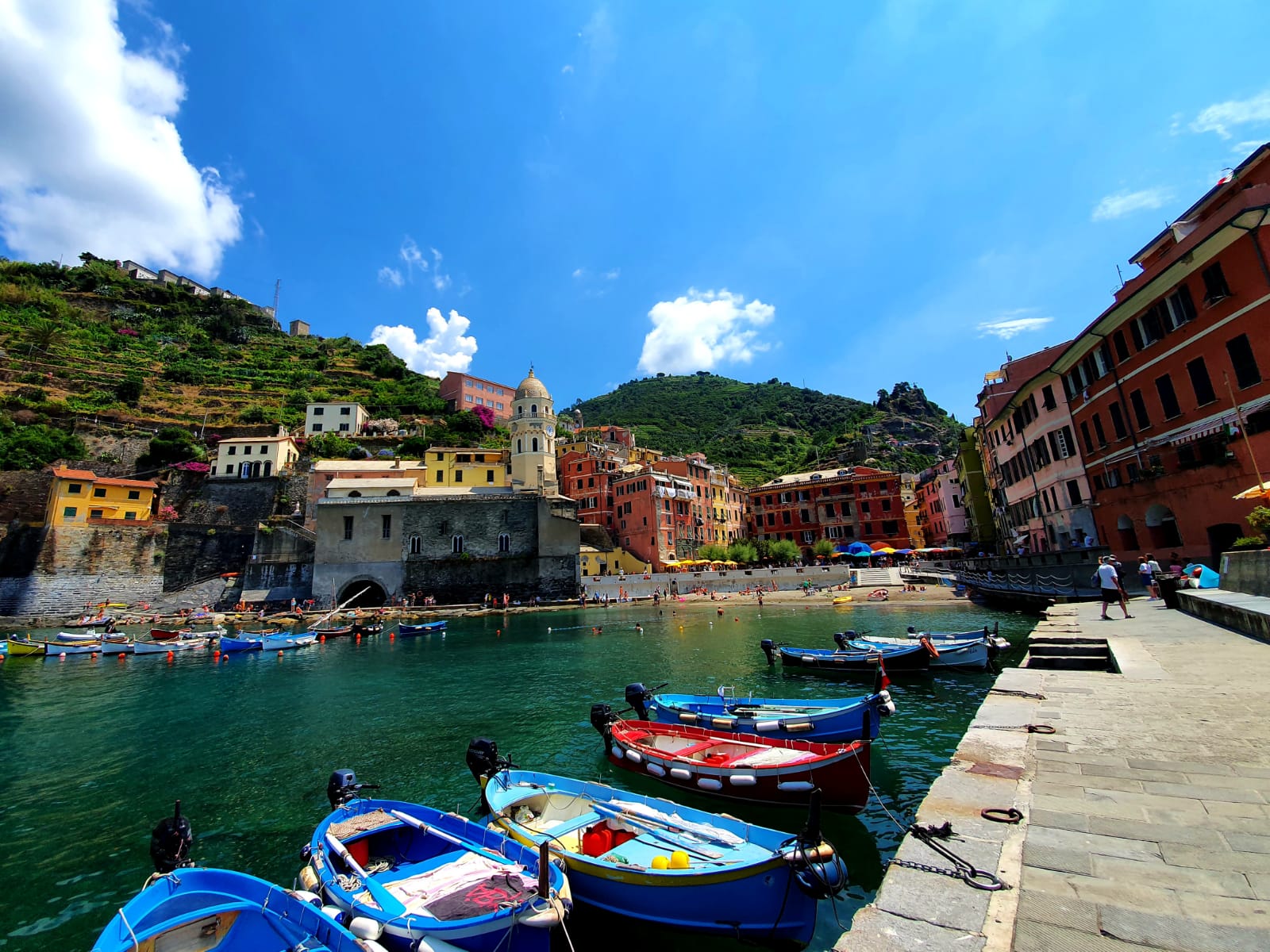 Boten liggen aangemeerd in de haven van Vernazza, Italië. Kleurrijke gebouwen onder een blauwe hemel. Cinque terre