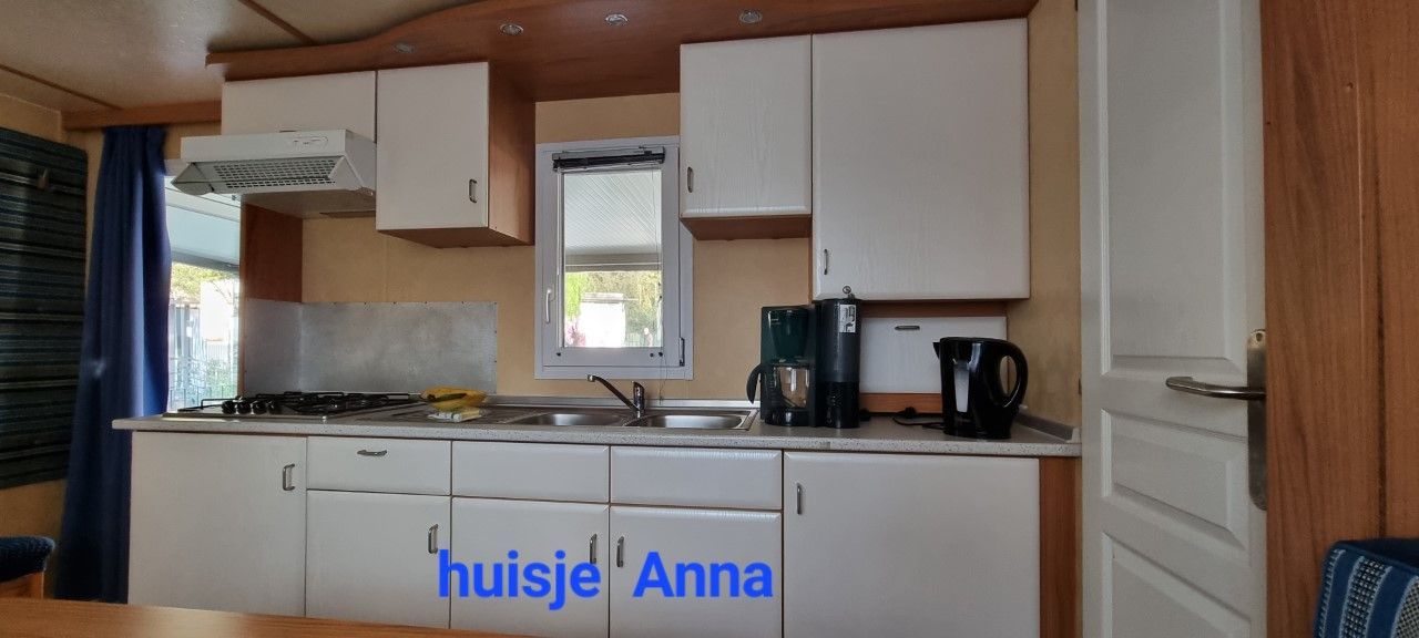 Keuken met witte kastjes, fornuis, spoelbak en koffiezetapparaat.