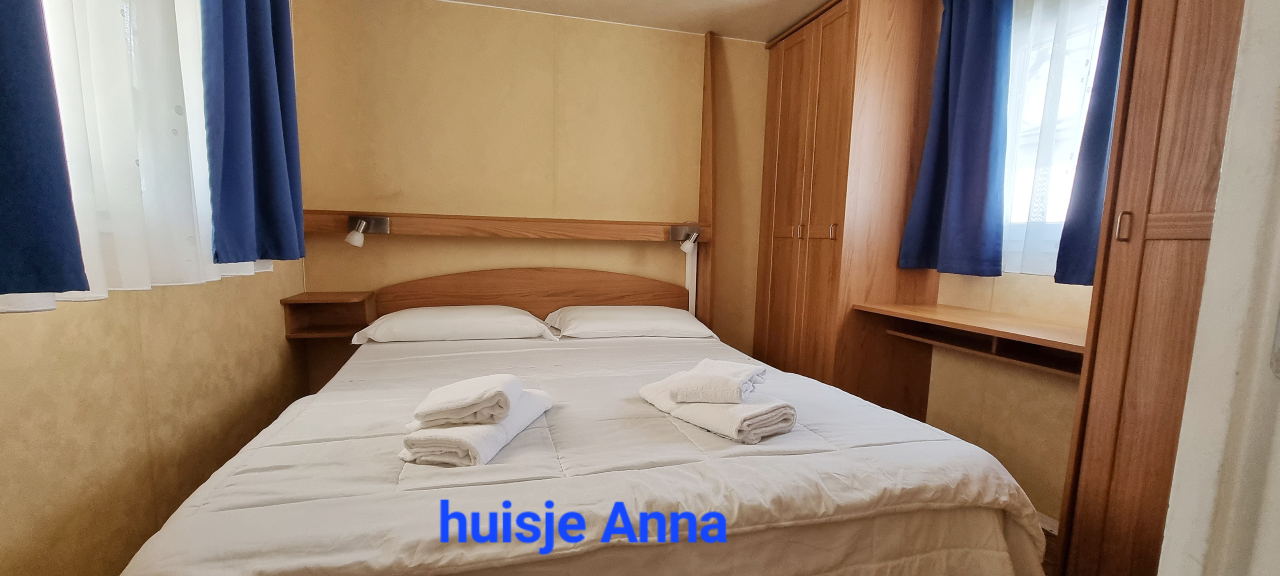 Slaapkamer met tweepersoonsbed, twee opgevouwen handdoeken, houten meubels, blauwe gordijnen.