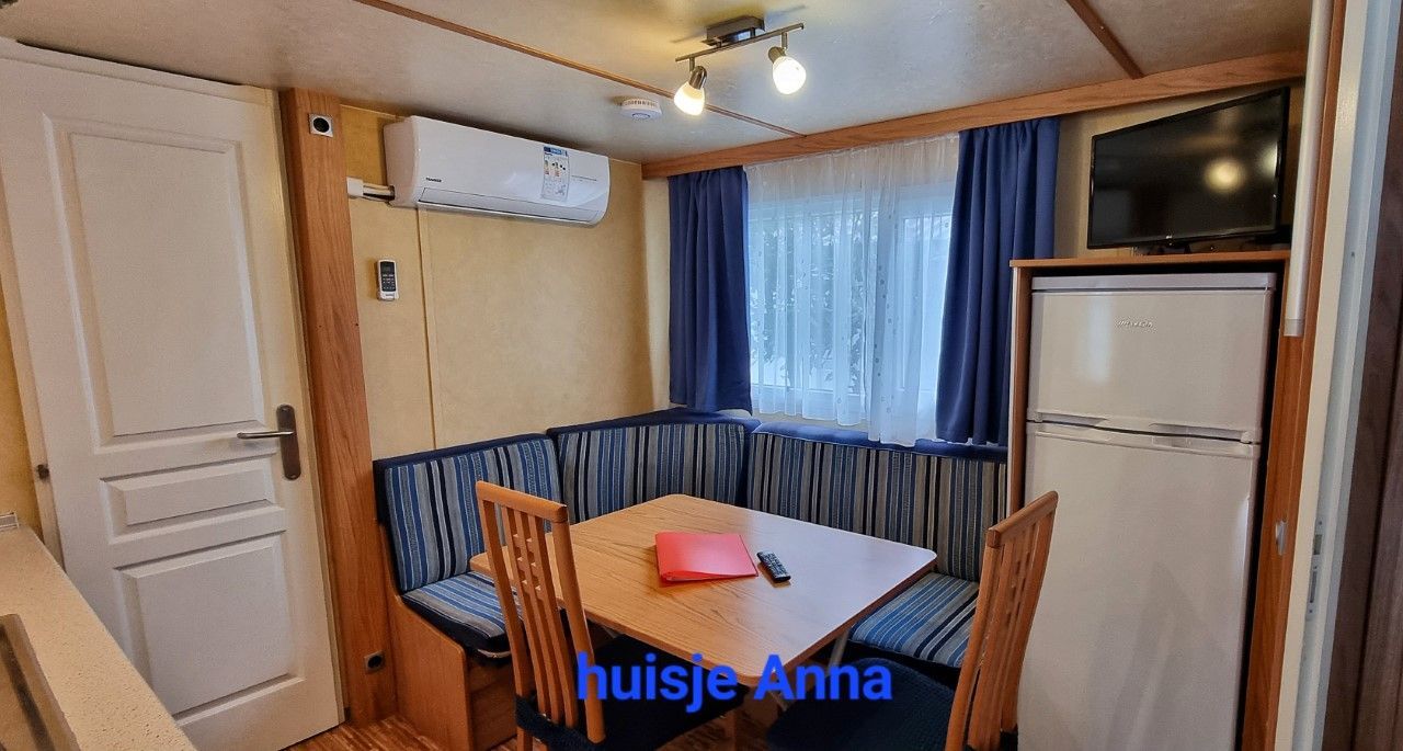 Interieur van een chalet Anna met tafel, zitgelegenheid, koelkast, raam en tv.