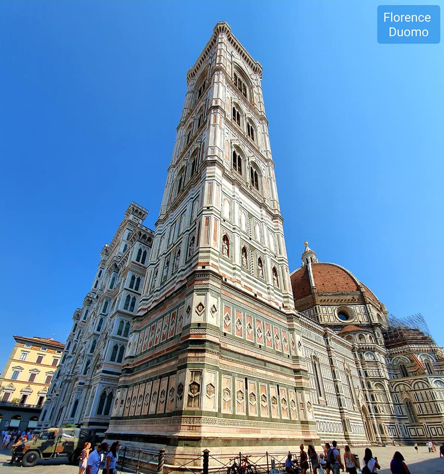 De Dom van Florence met zijn hoge, sierlijke klokkentoren en koepel tegen een helderblauwe hemel.