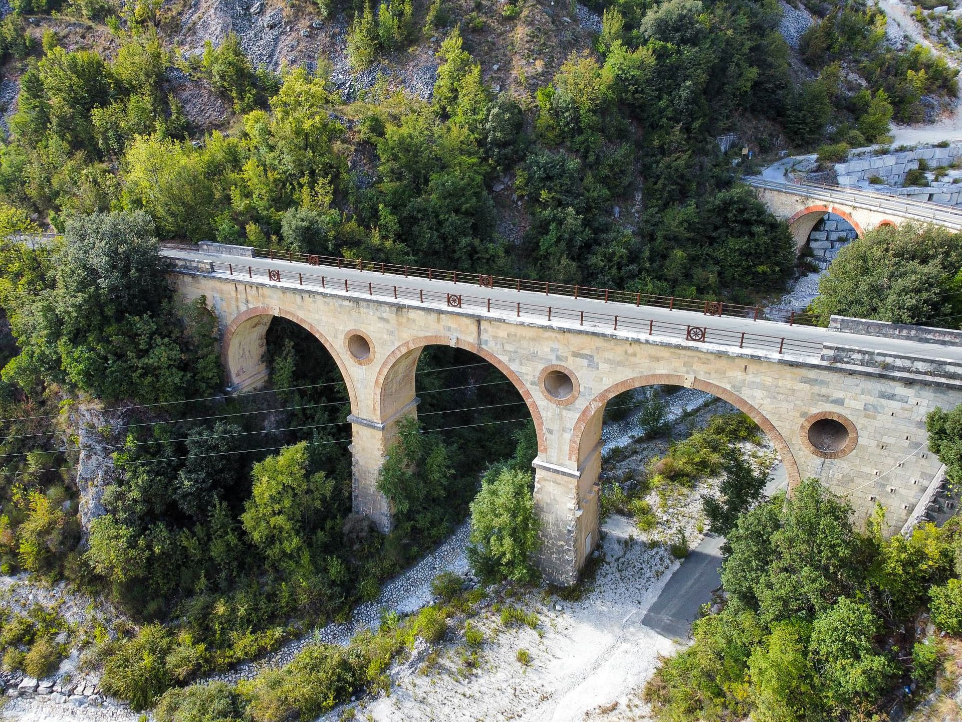 Een stenen boogbrug overspant een weelderige, groene vallei. Marmergroeven Carrara
