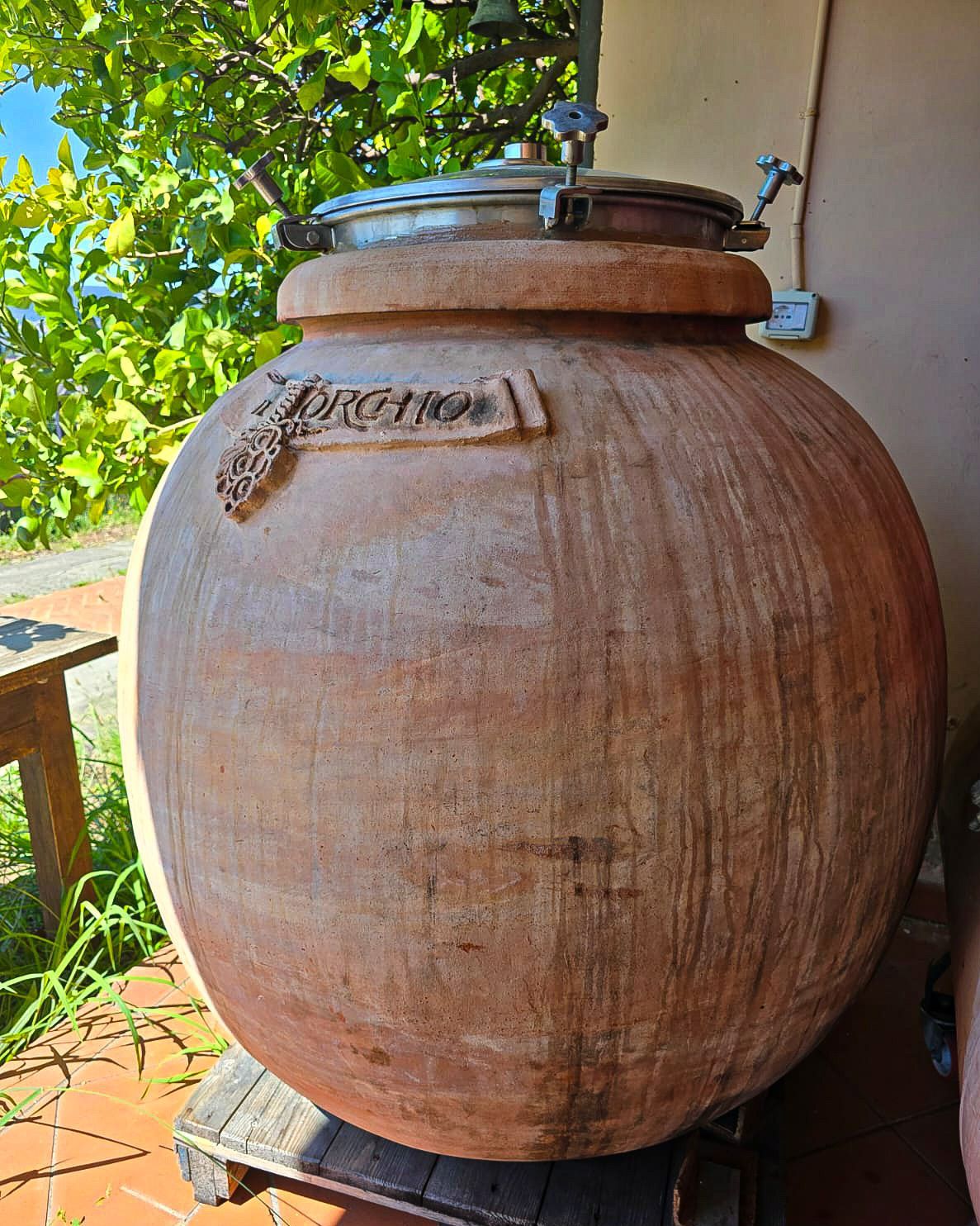 Grote terracotta fermentatieketel met metalen deksel, geplaatst op een houten platform il Torchio wijnproducent