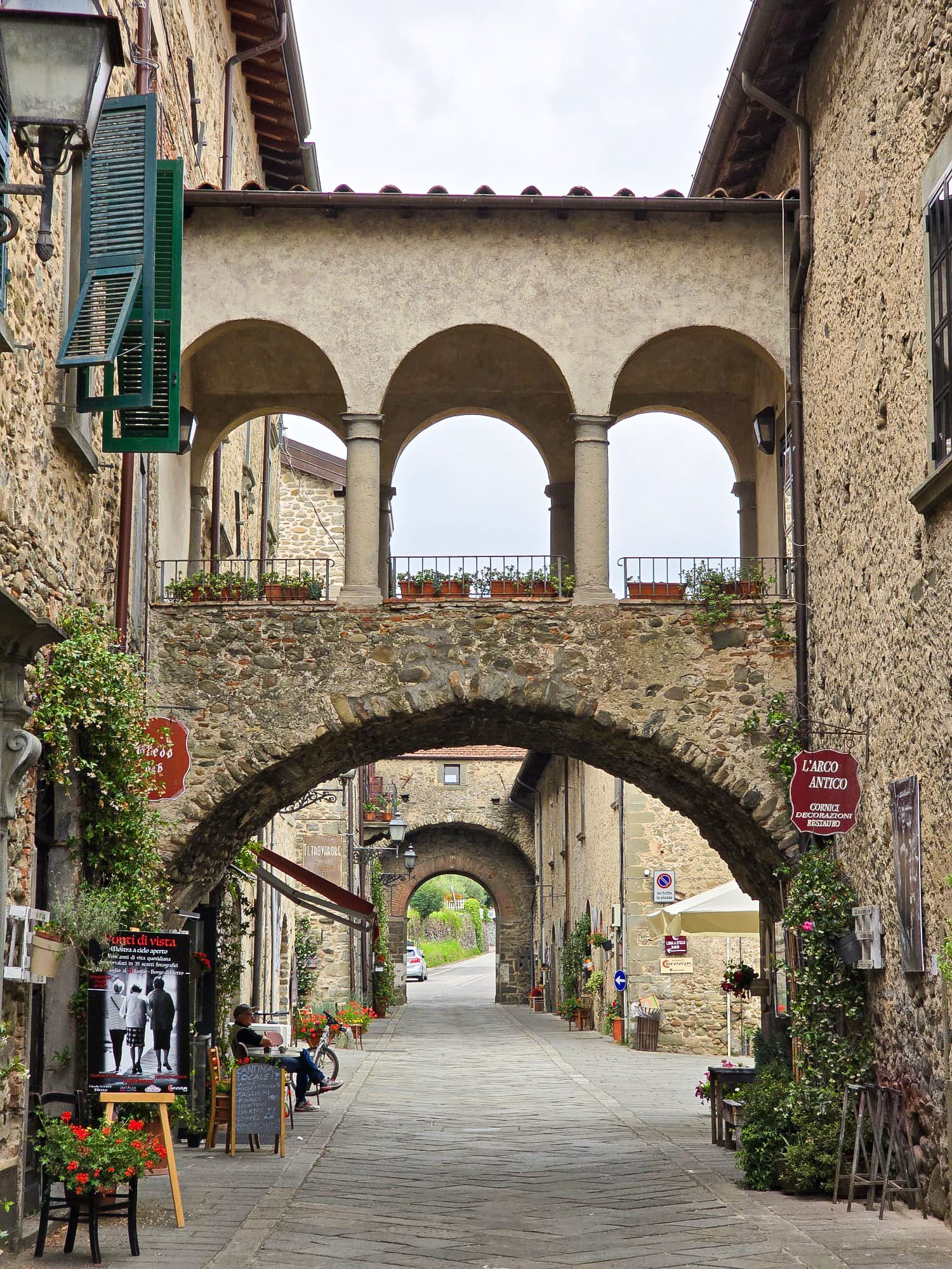 Stenen boog in een straatje van een Italiaans dorp, met daarboven een gebogen loopbrug.