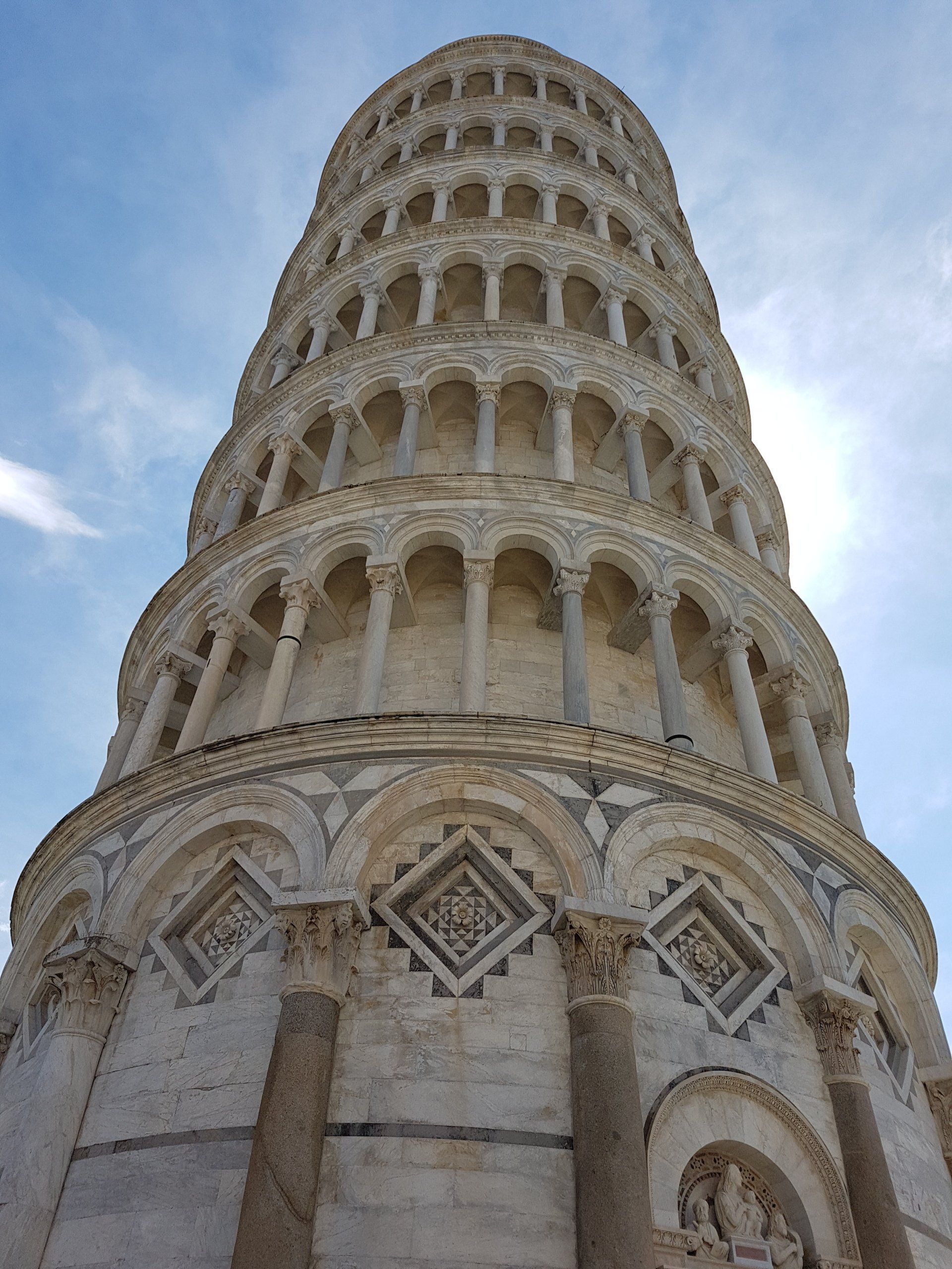De scheve toren van Pisa tegen een blauwe hemel, met zijn gedetailleerde architectonische versieringen en zuilen.