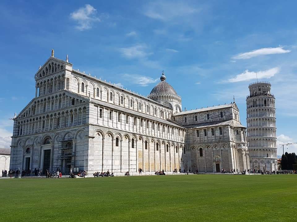 De kathedraal en de scheve toren van Pisa op een groen gazon onder een blauwe hemel.