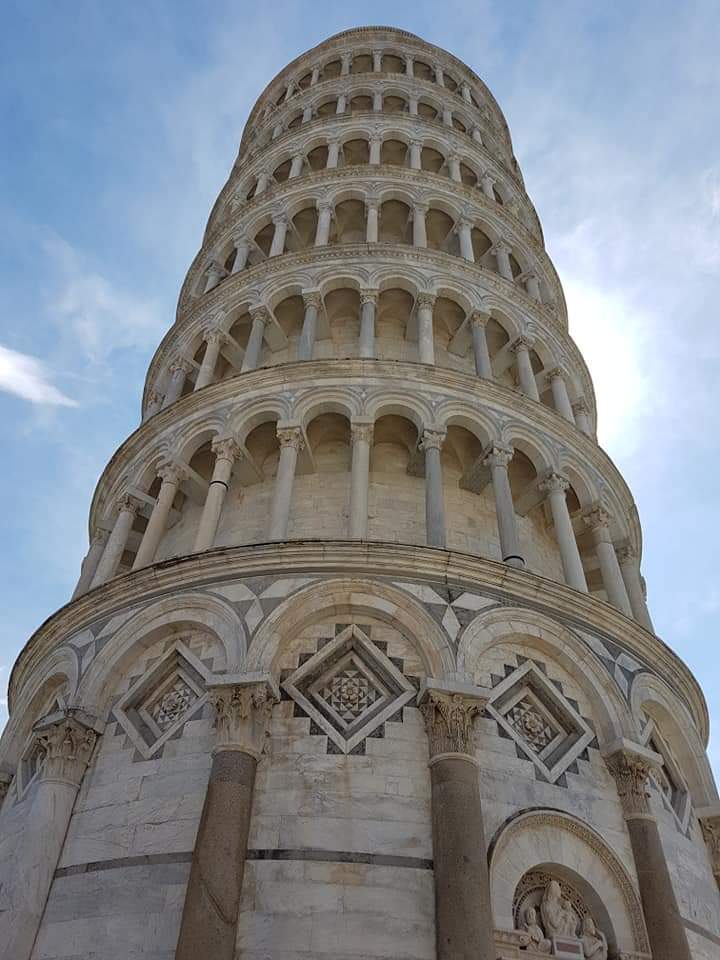 De scheve toren van Pisa, een witstenen bouwwerk tegen een gedeeltelijk bewolkte, blauwe hemel.