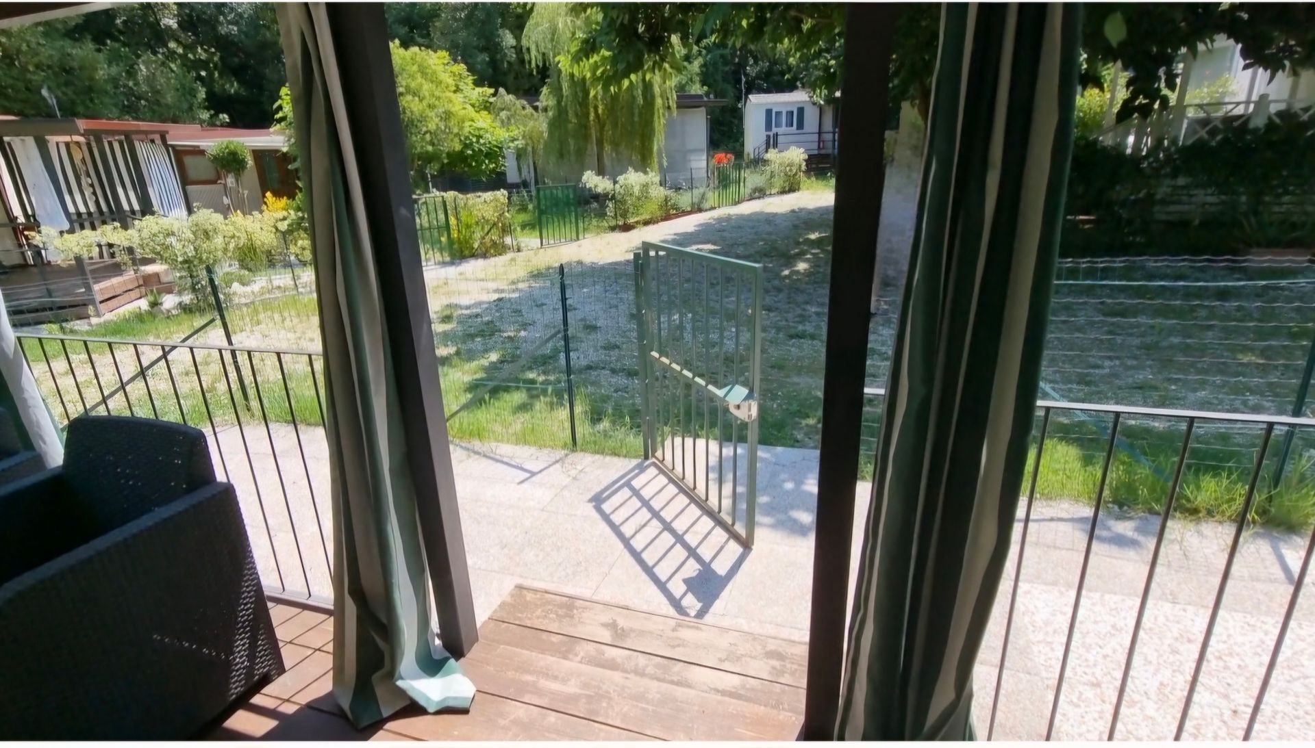 Uitzicht vanaf de veranda op een groene tuin met een hek en bomen.