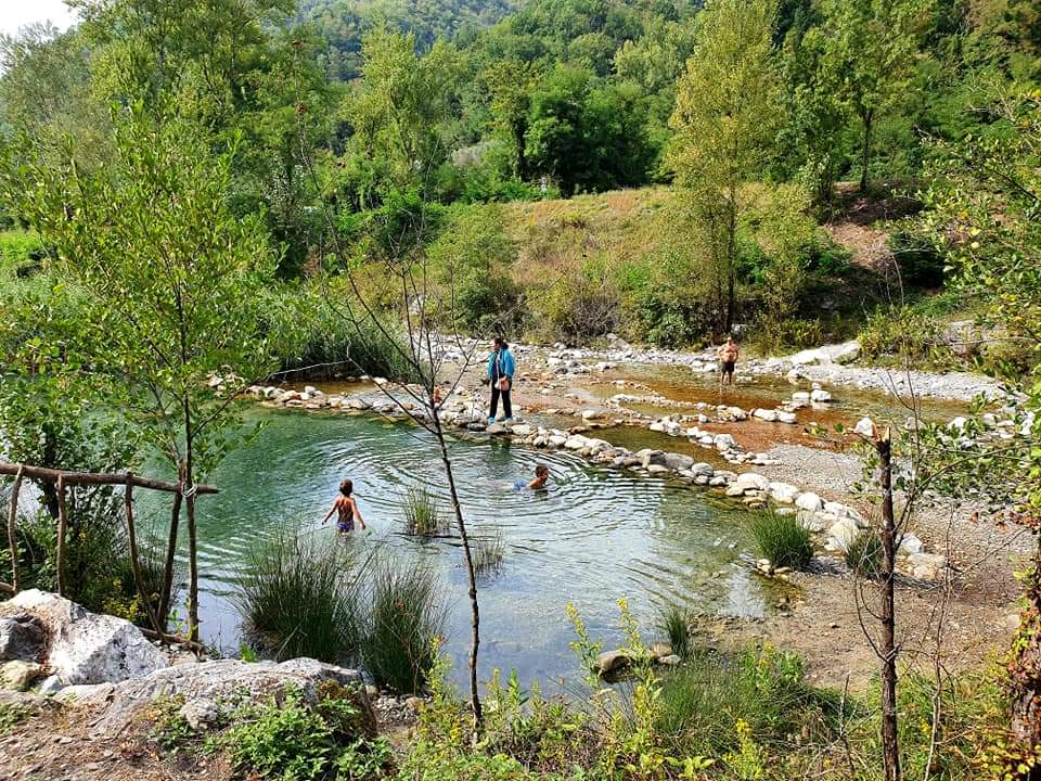 Equi terme: Mensen zwemmen in een heldere, ondiepe rivier, omgeven door bomen en vegetatie, op een zonnige dag.