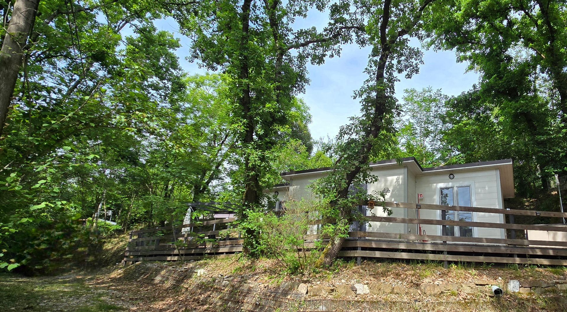 Ruim, modern ingericht chalet met houten veranda en bomen.