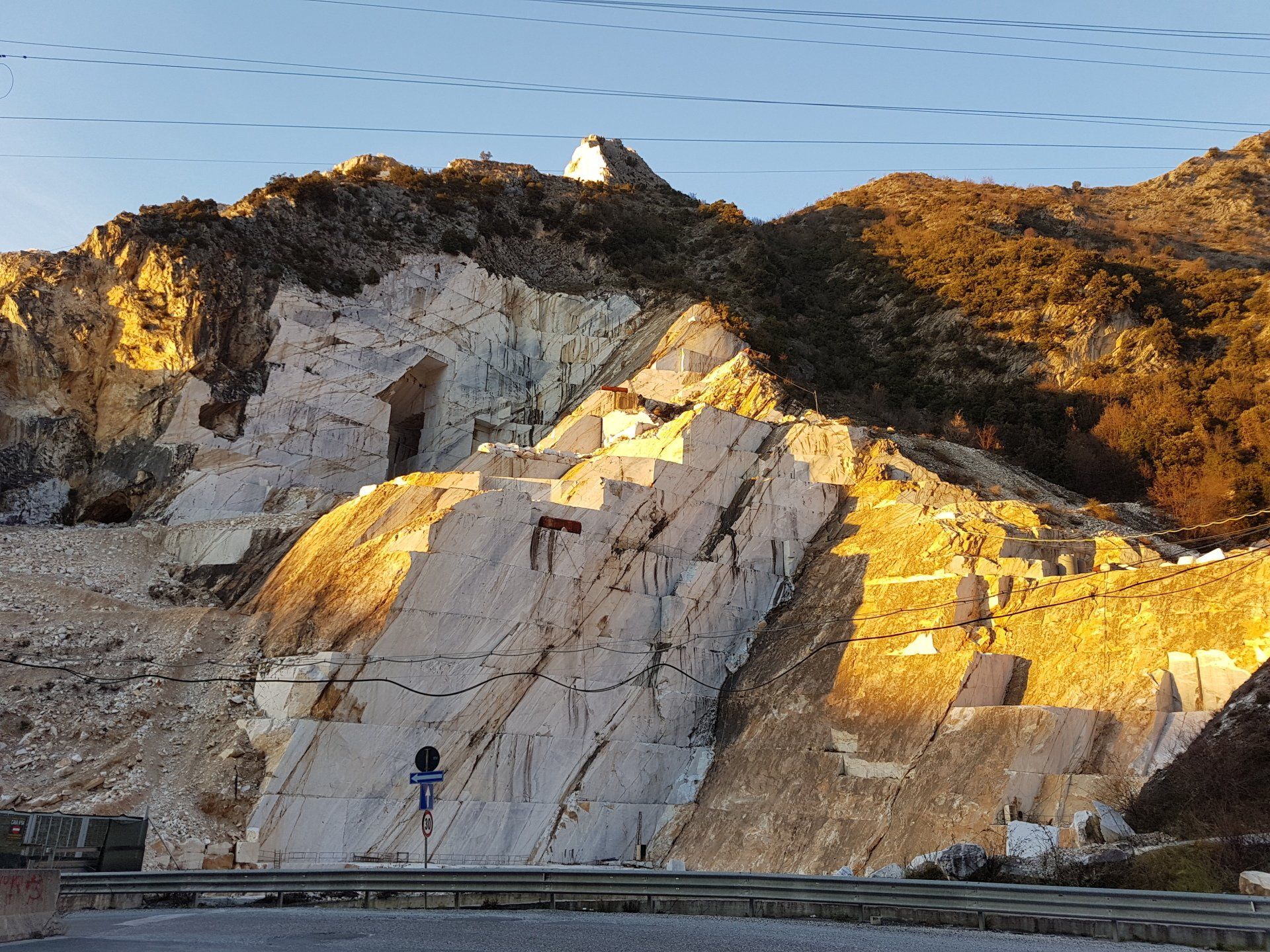 Marmergroeve in een bergachtig landschap, waar zonlicht de witte rotswanden en de omringende heuvels verlicht. Carrara