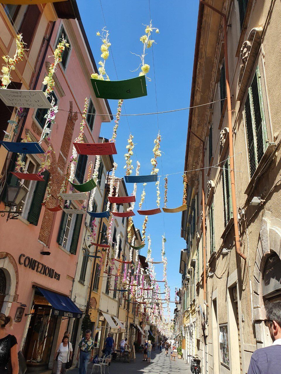 Een smalle straat met kleurrijke gebouwen en decoratieve slingers op een zonnige dag. Pietrasanta