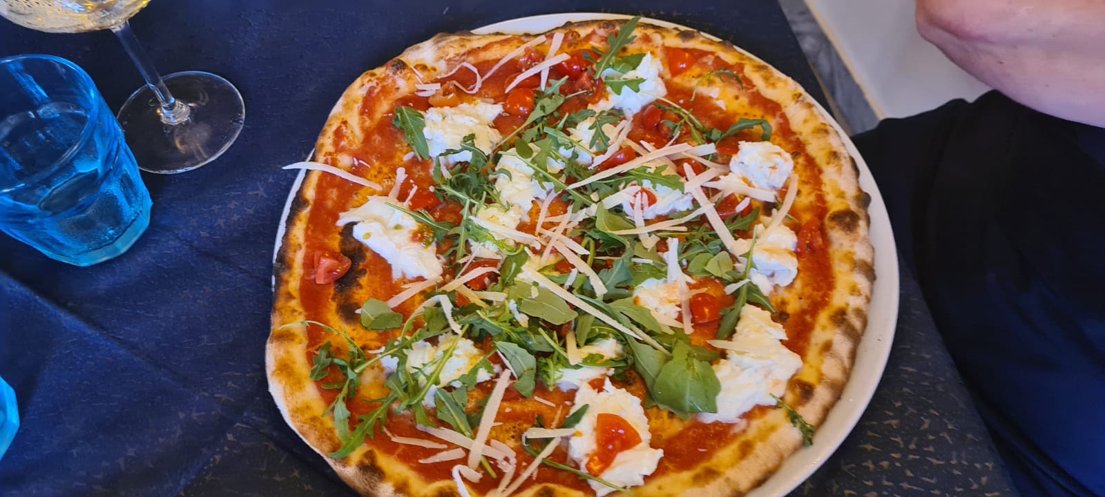 Pizza met diverse toppings, waaronder rucola en kaas, op een wit bord.