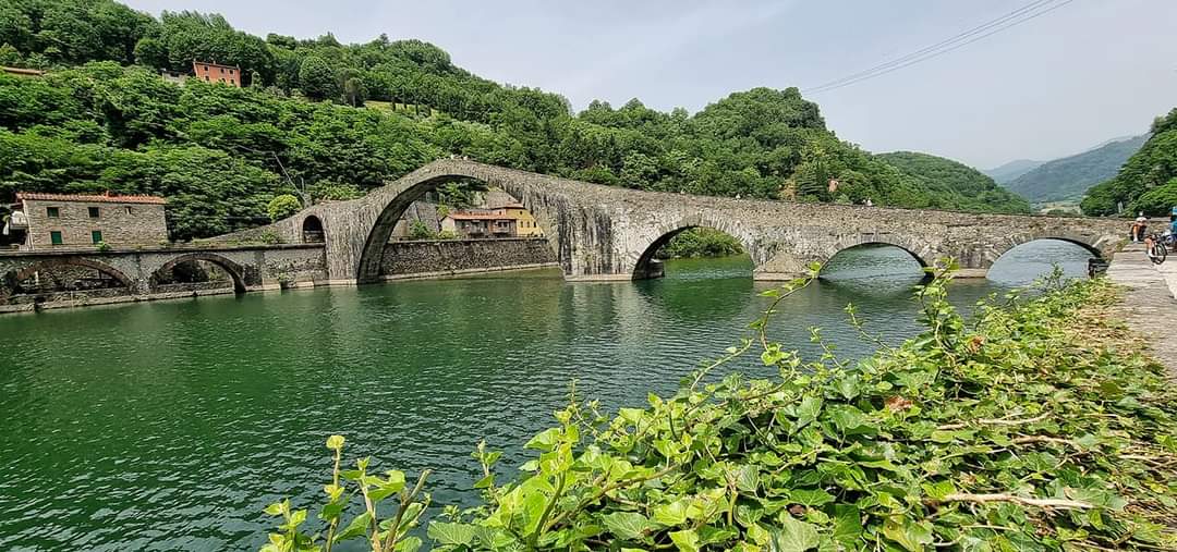 Een stenen brug overspant een groene rivier, ponte del diavolo