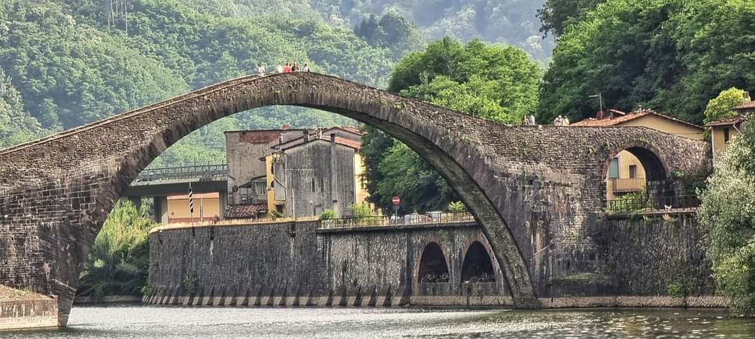 Stenen boogbrug over het water met gebouwen en groen op de achtergrond. Pontedel diavolo