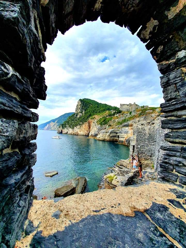 Uitzicht op turquoise water en kustkliffen omlijst door een stenen boog. Portovenere