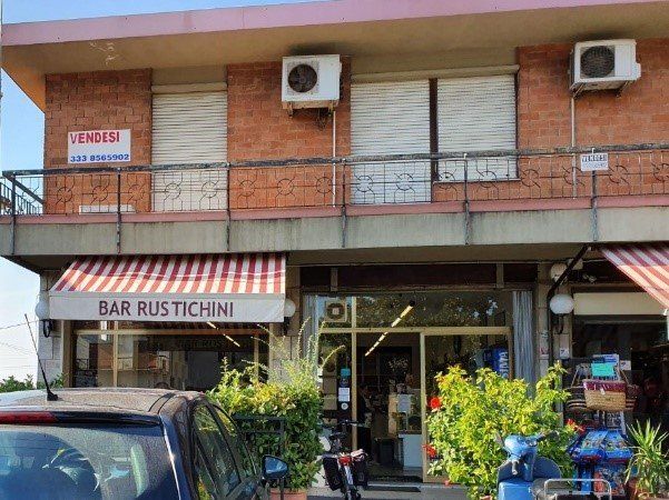 Bar Rustichini met een rood-wit gestreepte luifel. Gebouw met gesloten ramen op de bovenverdieping en een