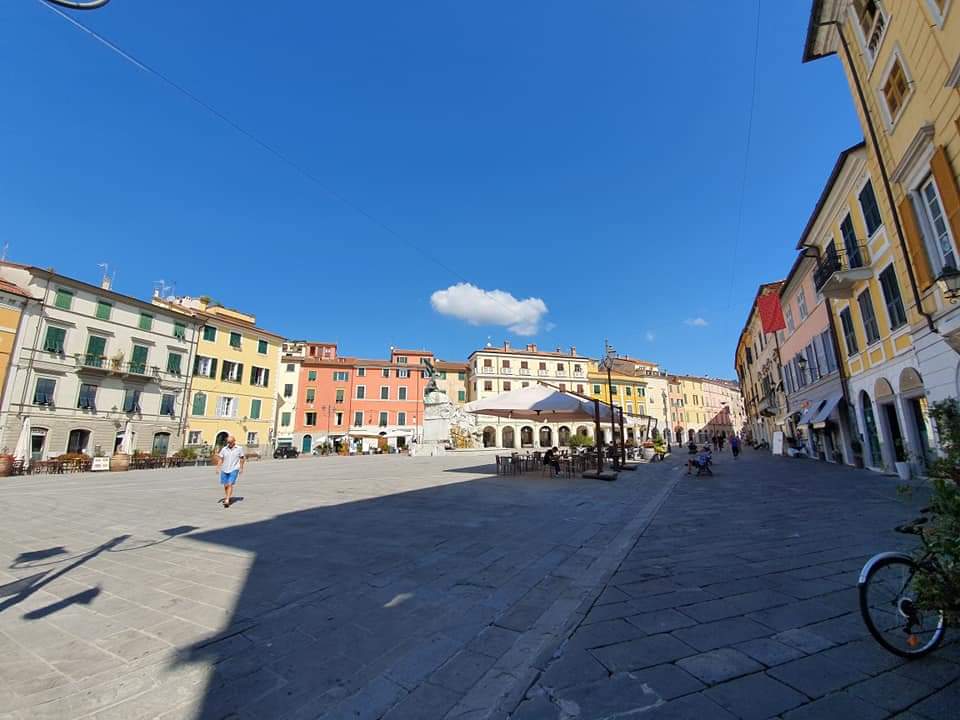 Groot geplaveid plein, kleurrijke gebouwen, zonnige dag. Sarzana