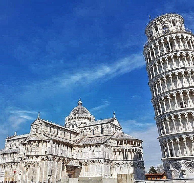 De scheve toren van Pisa en de kathedraal van Pisa tegen een blauwe hemel. Witte stenen gebouwen.