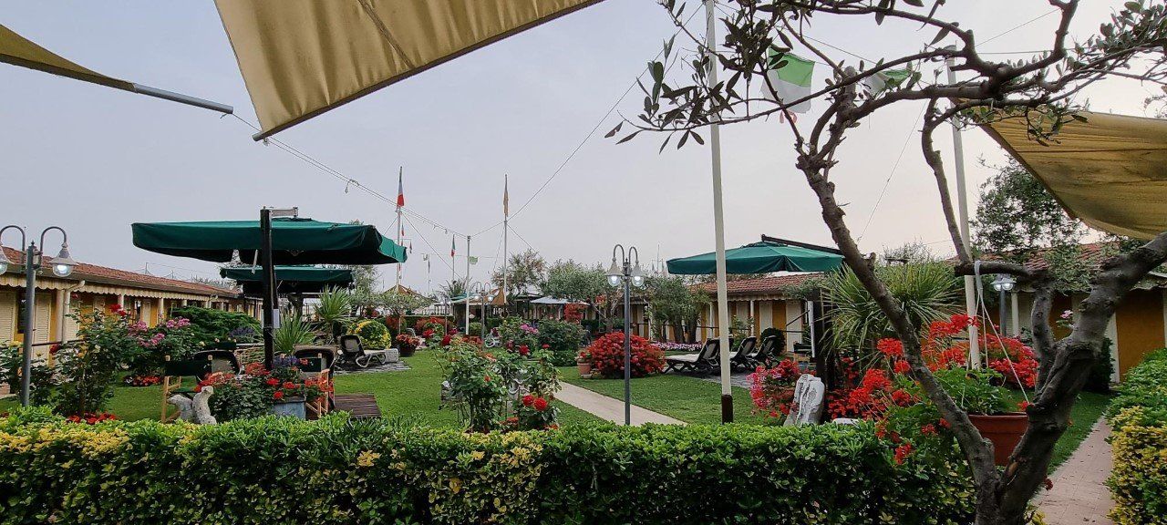 Een eethoek in de tuin met tafels, parasols, bloemen en een boom, mogelijk bij een restaurant.