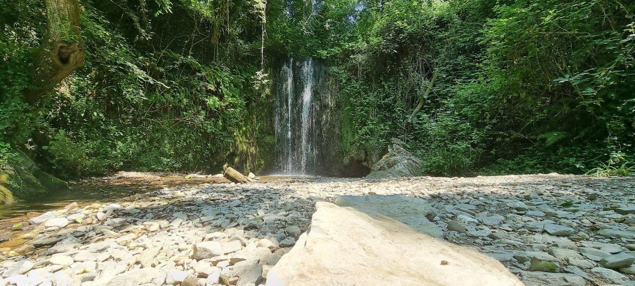Een waterval die neerstort in een rotsachtige beek, omgeven door weelderig groen.
