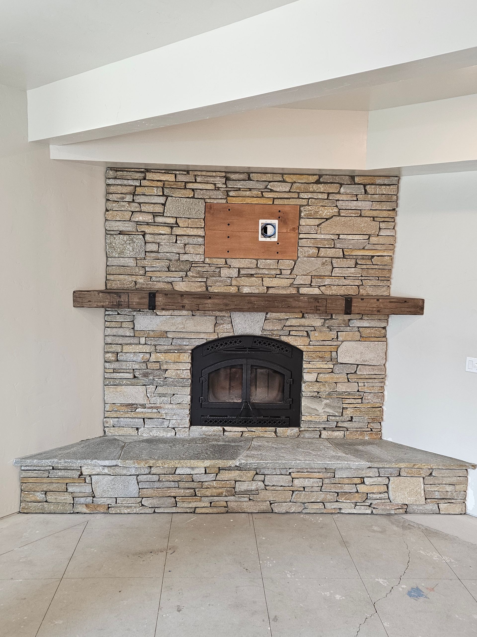 A stone fireplace with a wooden mantle in an empty room