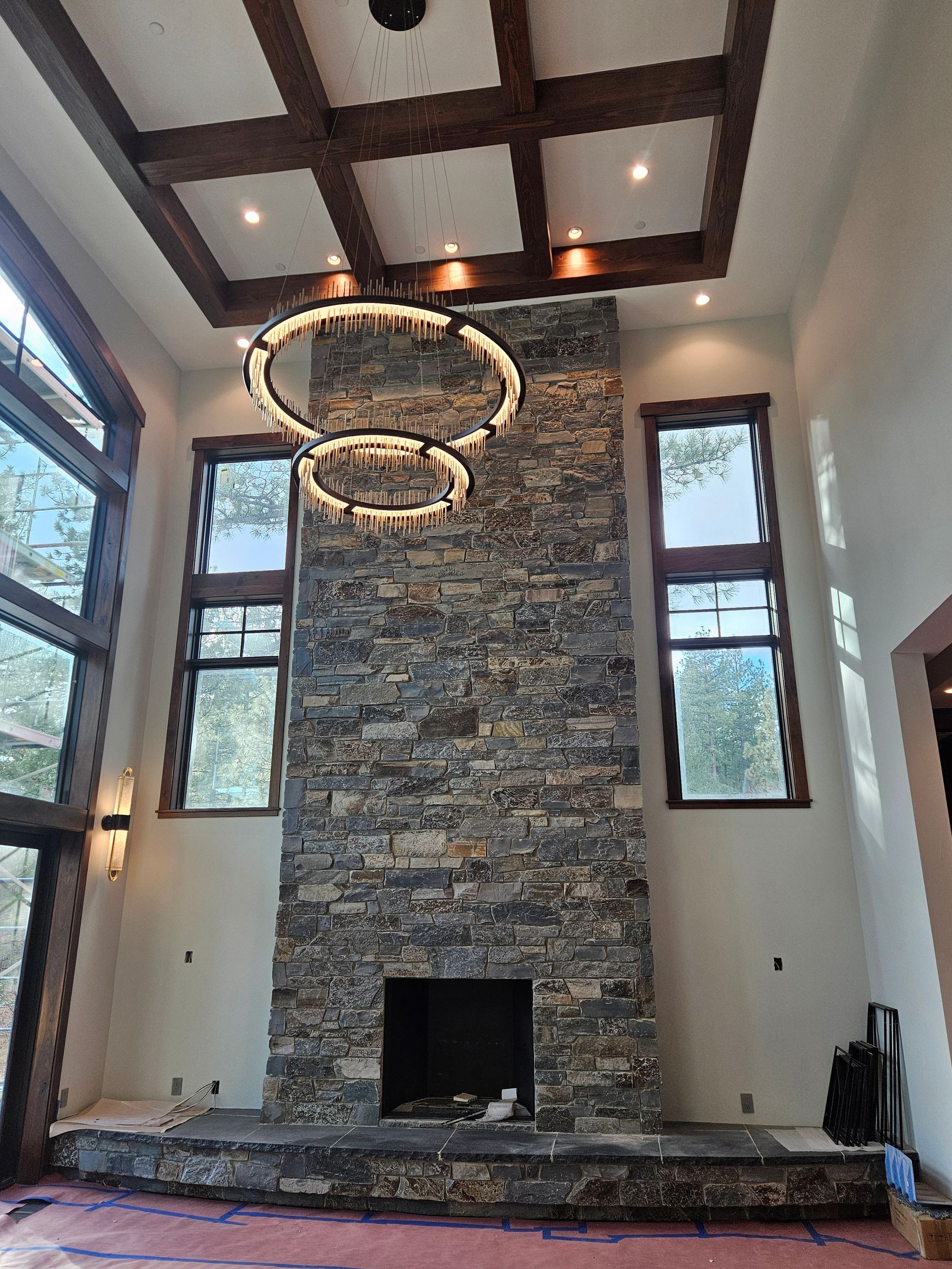 A living room with a large stone fireplace and a chandelier hanging from the ceiling
