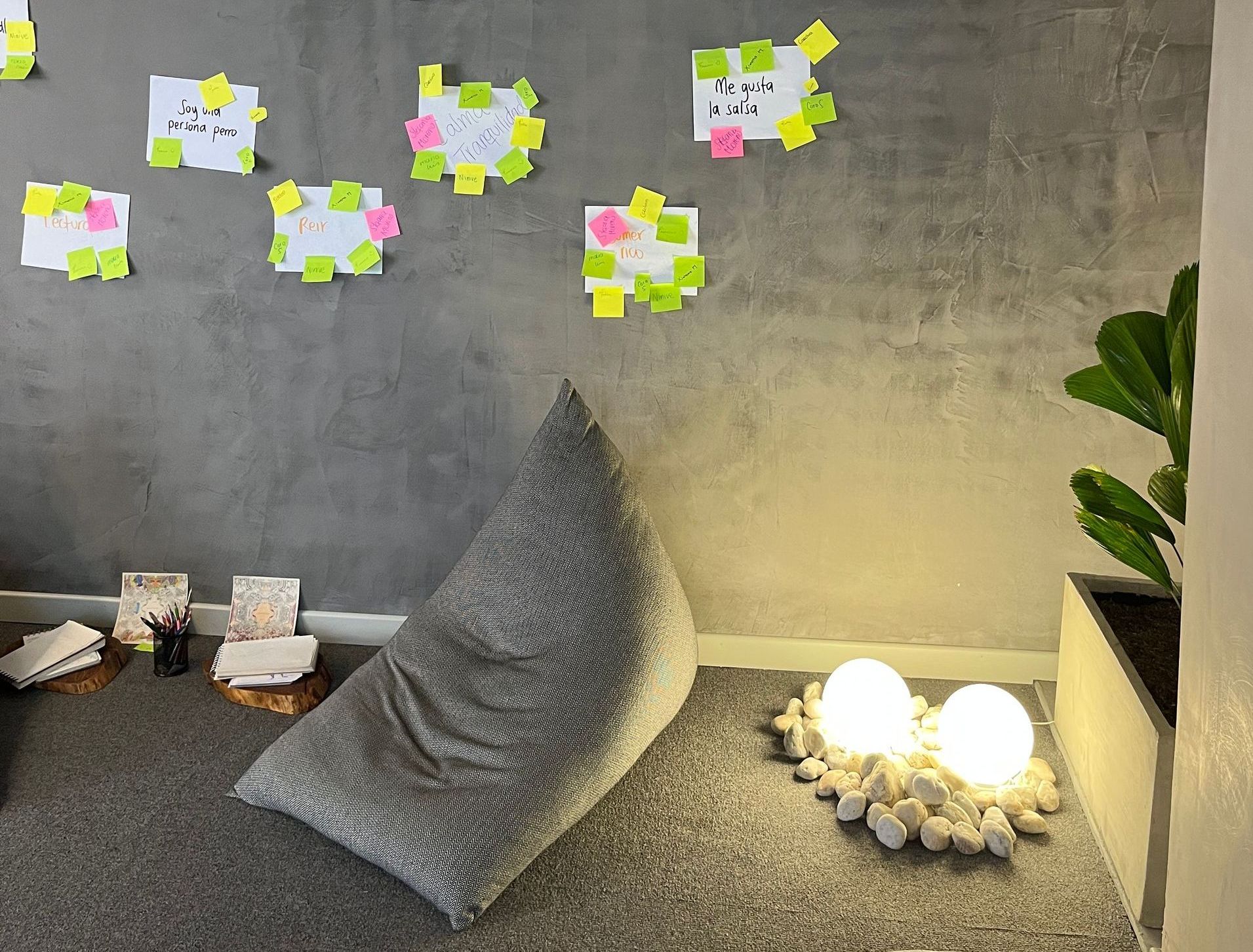 Sillón puf gris, luces de globo y plantas contra una pared de hormigón con notas adhesivas.