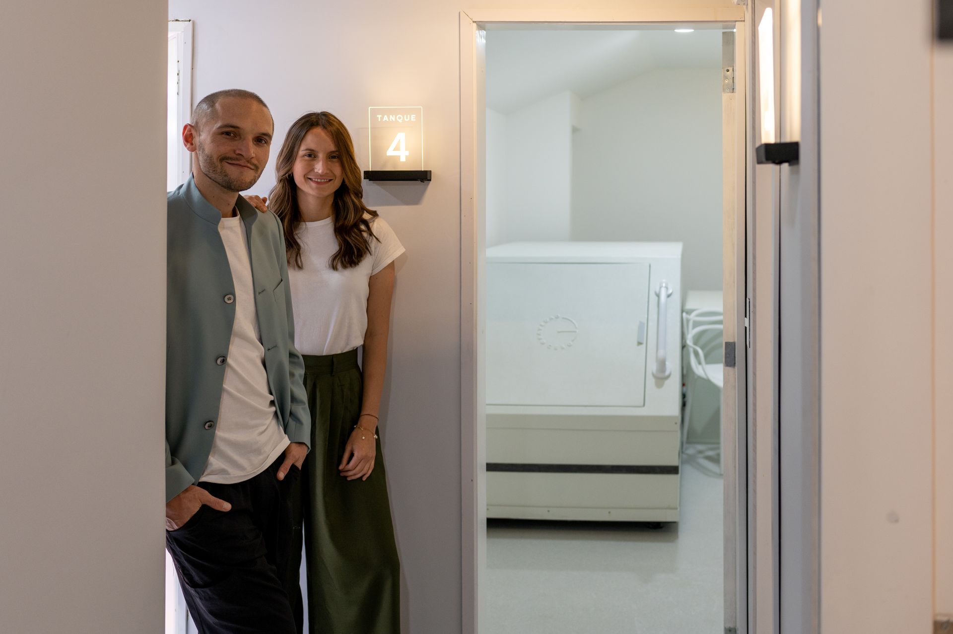 Una pareja sonríe, enmarcada por una puerta, con una caja fuerte visible en la habitación detrás de ellos.