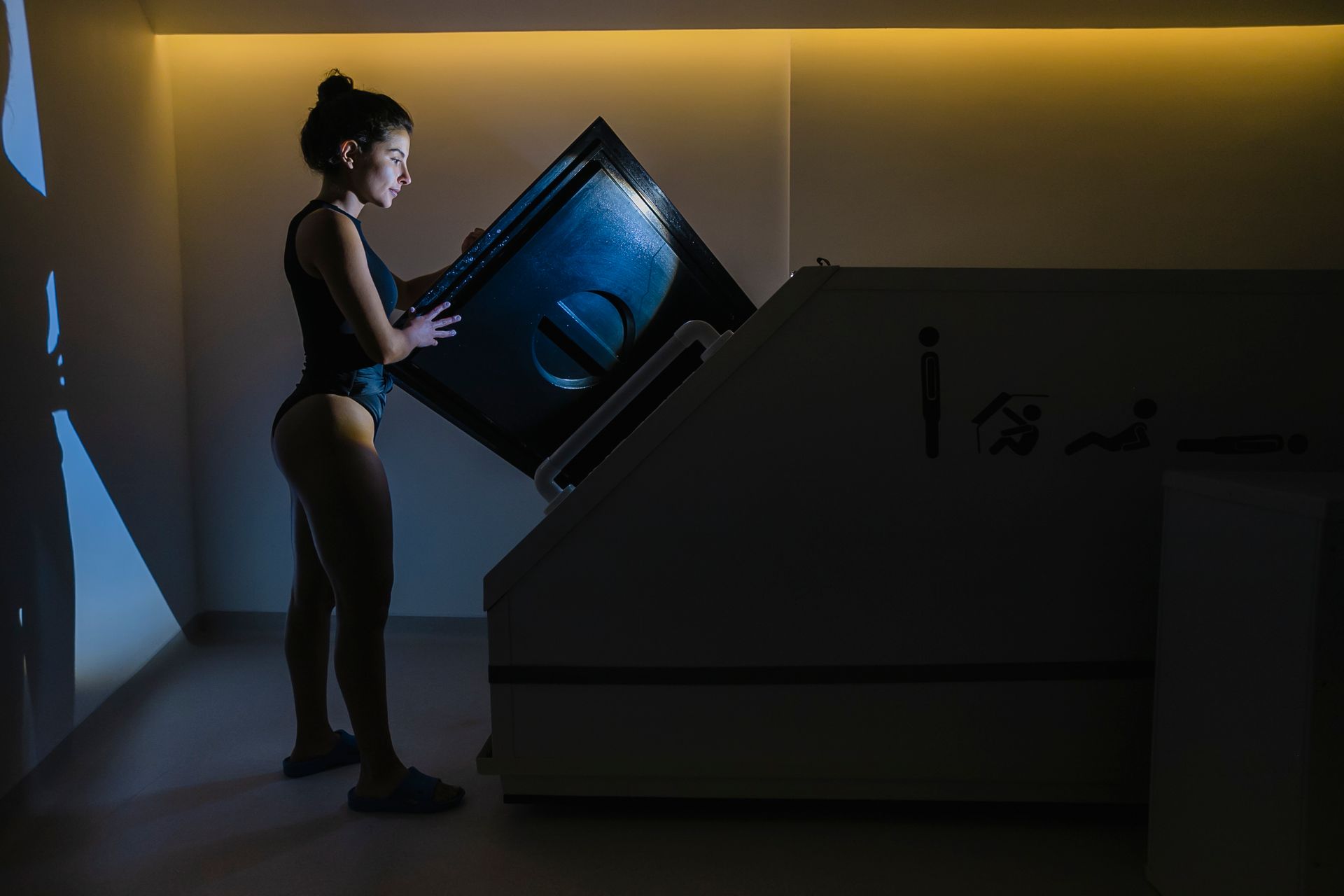 Mujer abriendo la puerta del tanque de flotación en una habitación poco iluminada.