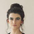 Mujer con cabello oscuro recogido en un moño, con sombra de ojos azul, mirando a la cámara.