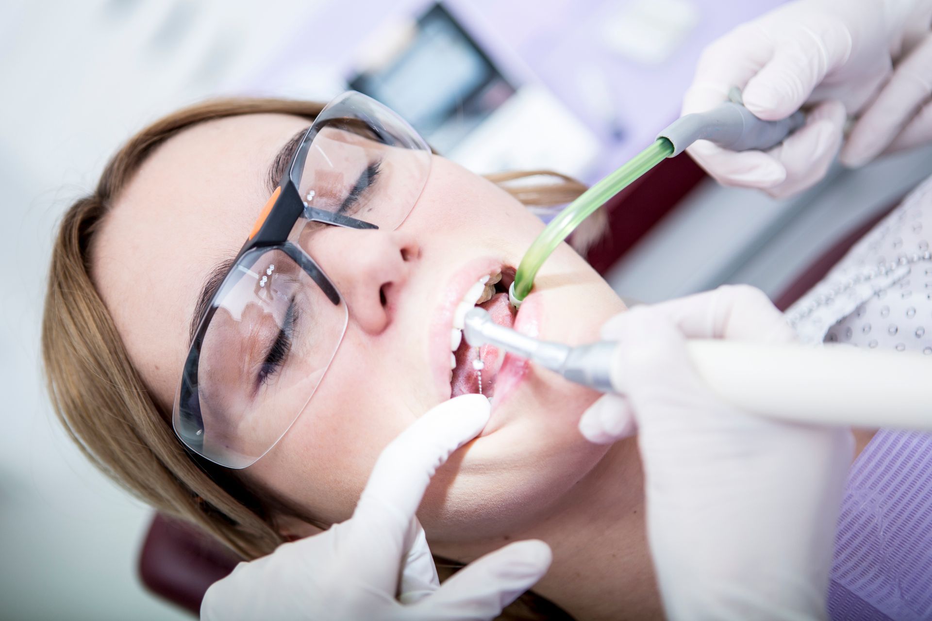 Dentista che esamina la bocca del paziente con uno specchio. Guanti blu, bocca spalancata, denti bianchi, in casa.