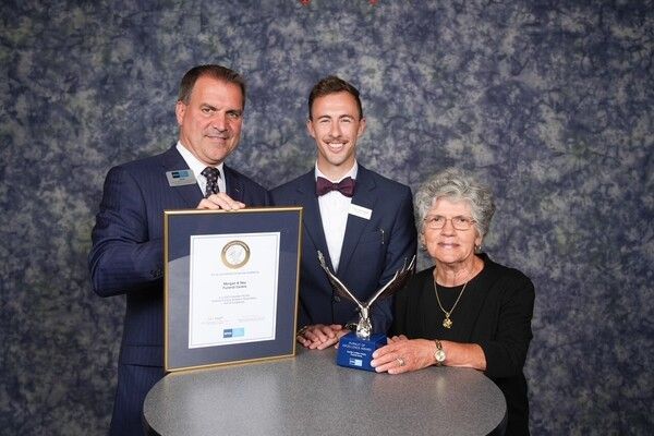 Three people pose with an award plaque and trophy at a formal ceremony.