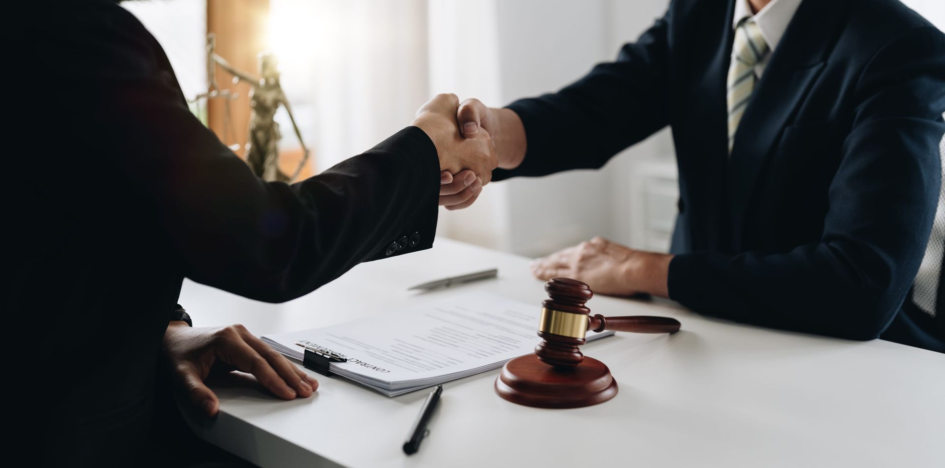 Two businesspeople shaking hands across a desk with a gavel in a law office.