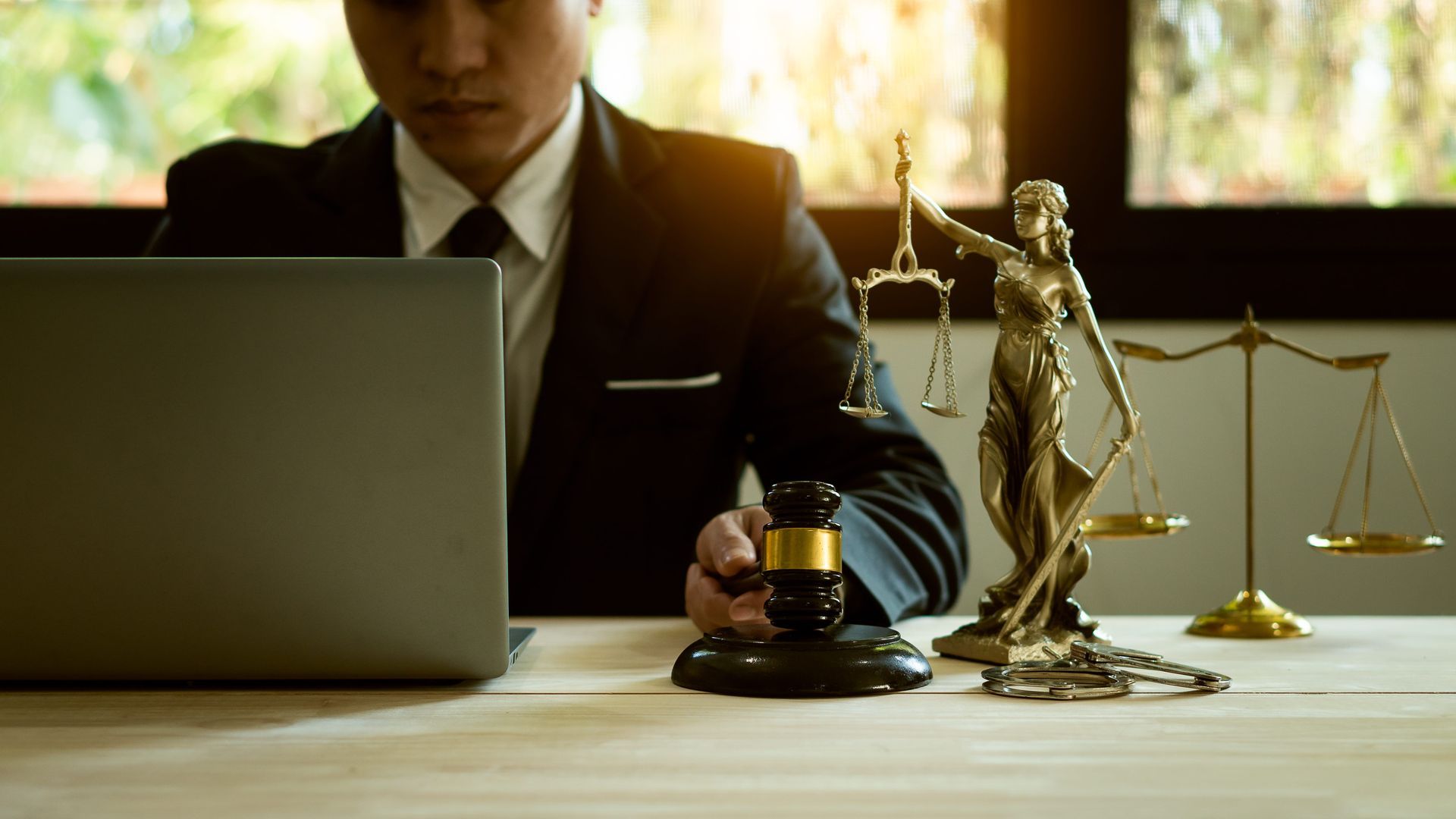 Professional on desk with laptop, legal scales, gavel, and Lady Justice statue
