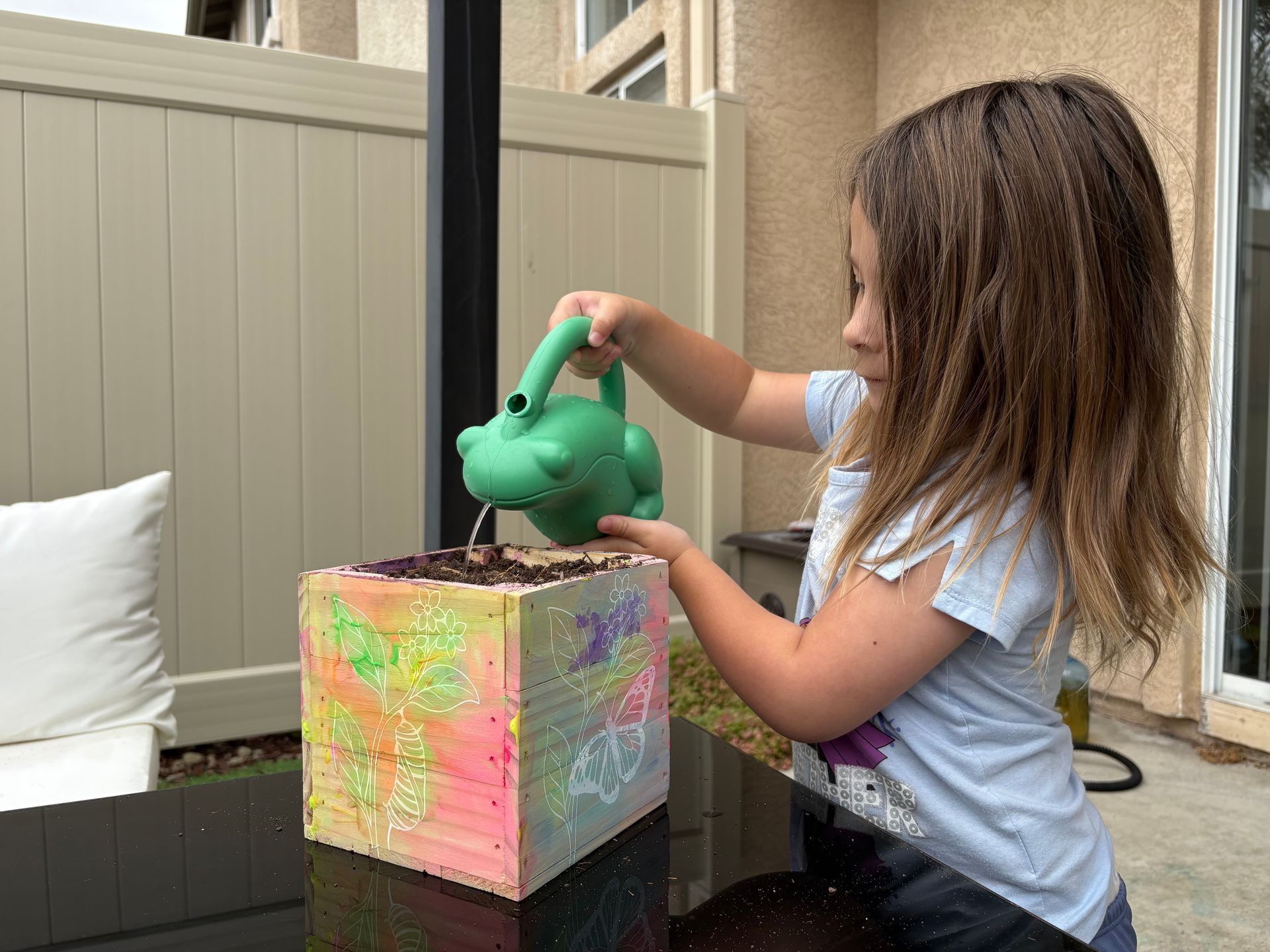 Girl watering a colorful planter box outdoors.