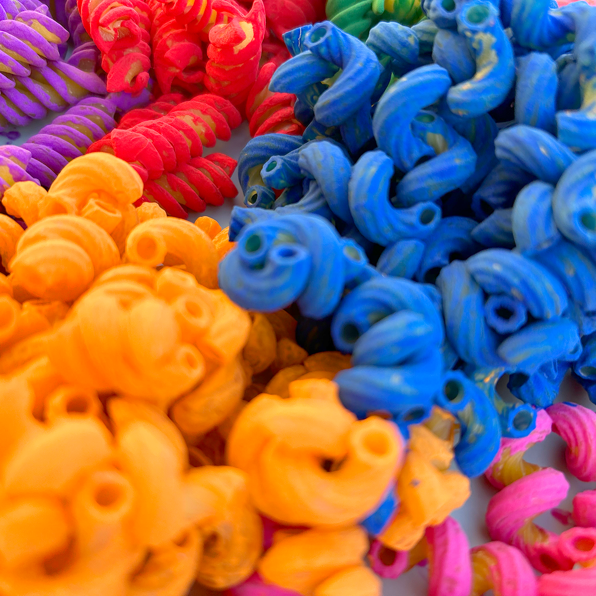 Close-up of colorful pasta in rainbow hues: red, orange, yellow, blue, pink, and purple.