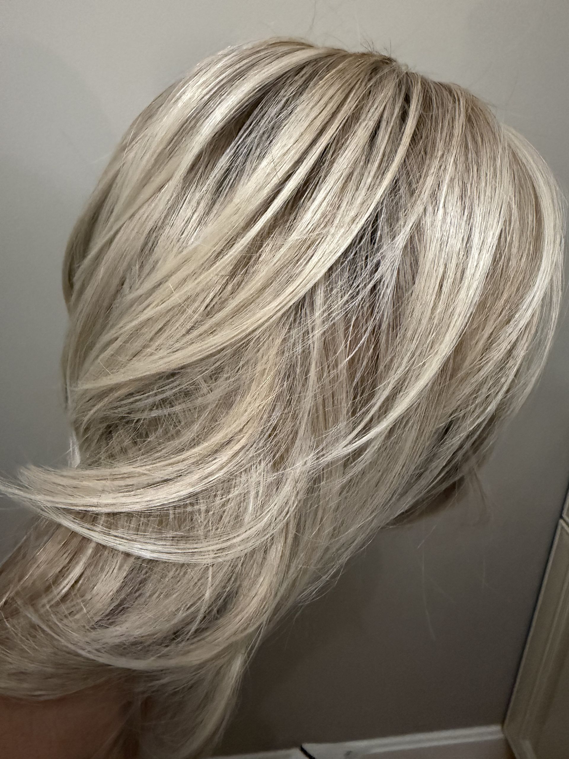 Short layered blonde haircut with dark roots, styled in soft swept-back waves.