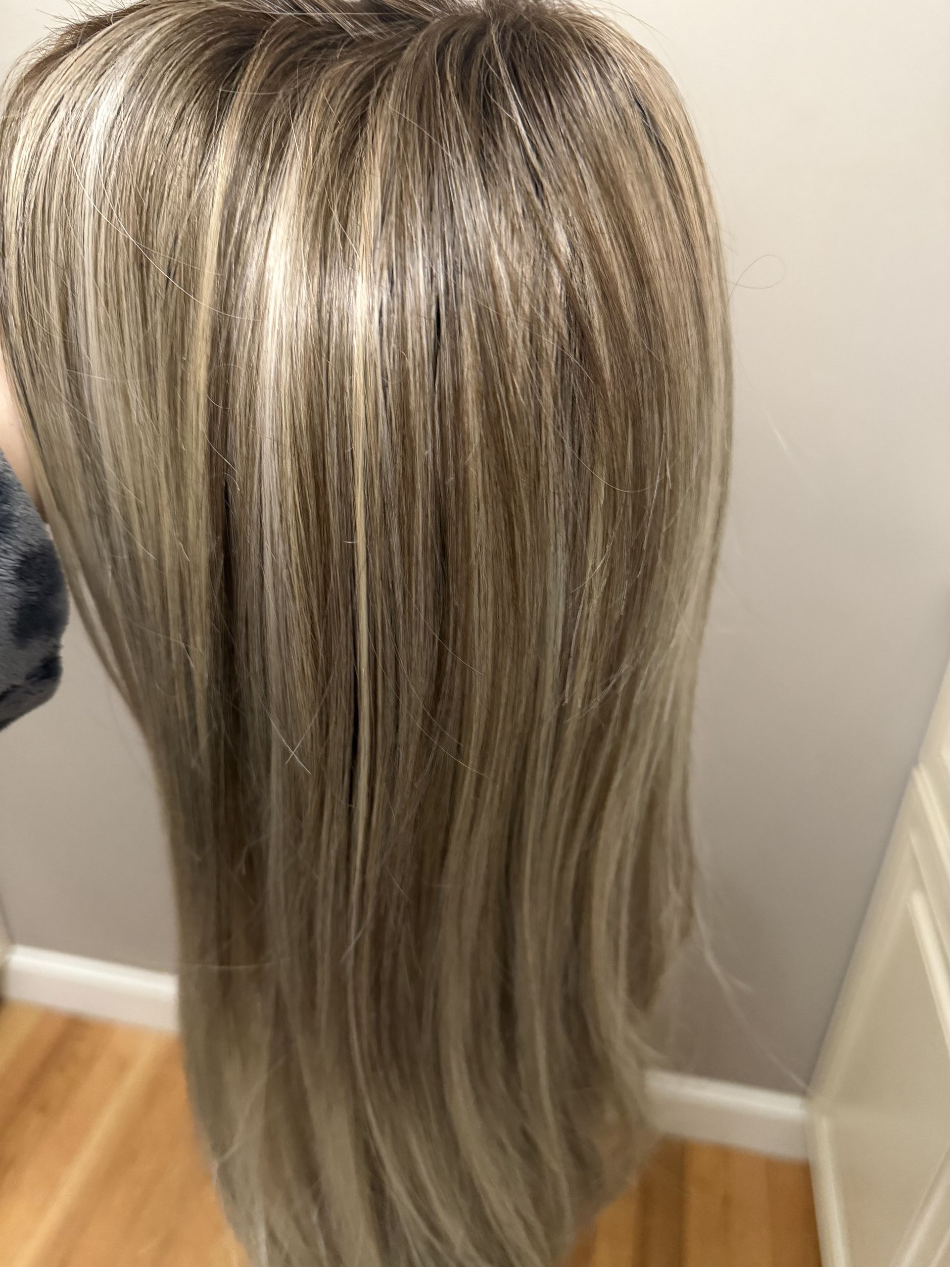 Long, layered blonde hair with ash-brown lowlights, shown from the back against a plain wall.