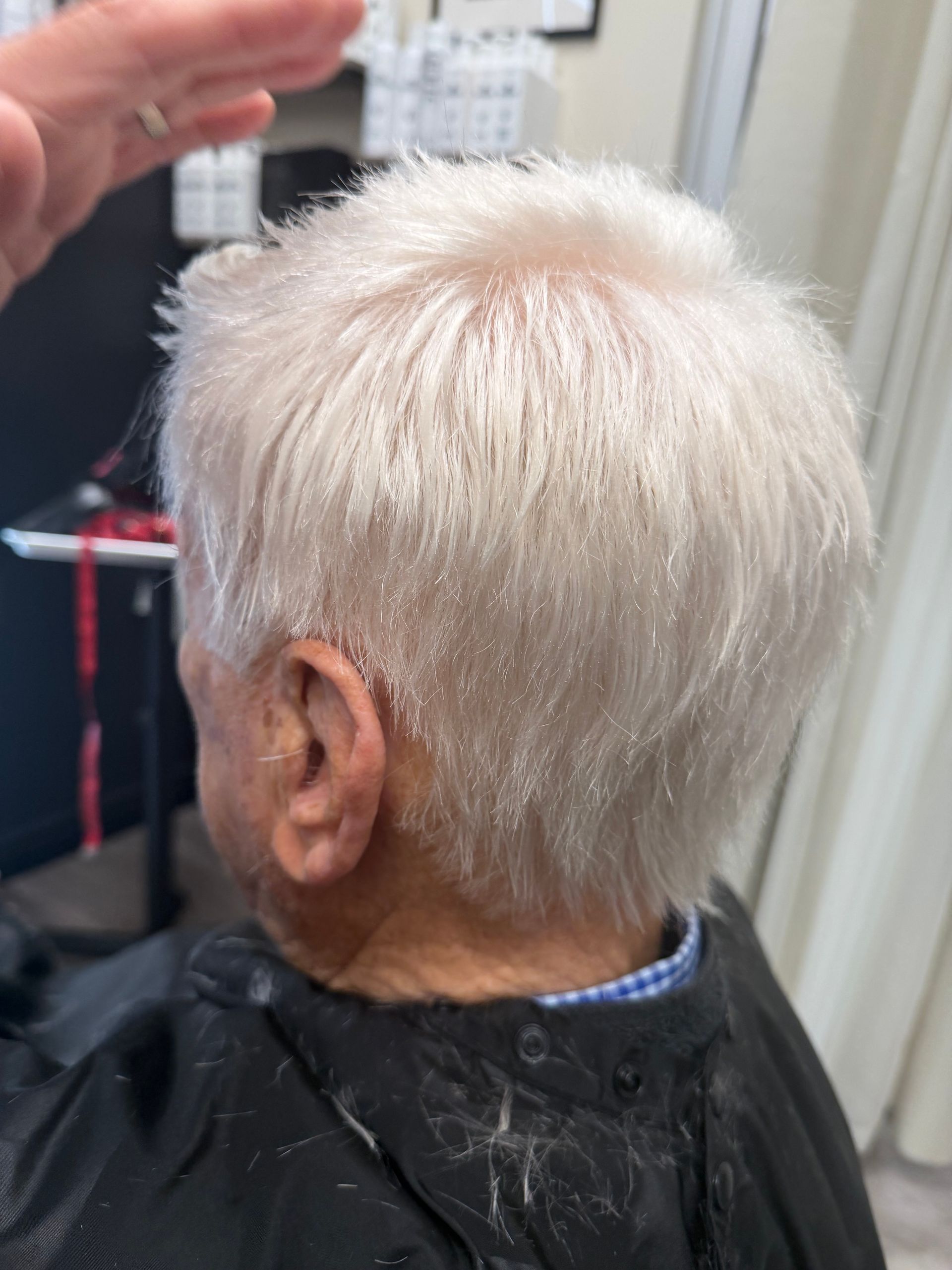 Woman getting hair styled, wearing a white shawl. Someone uses a brush and a hair dryer.