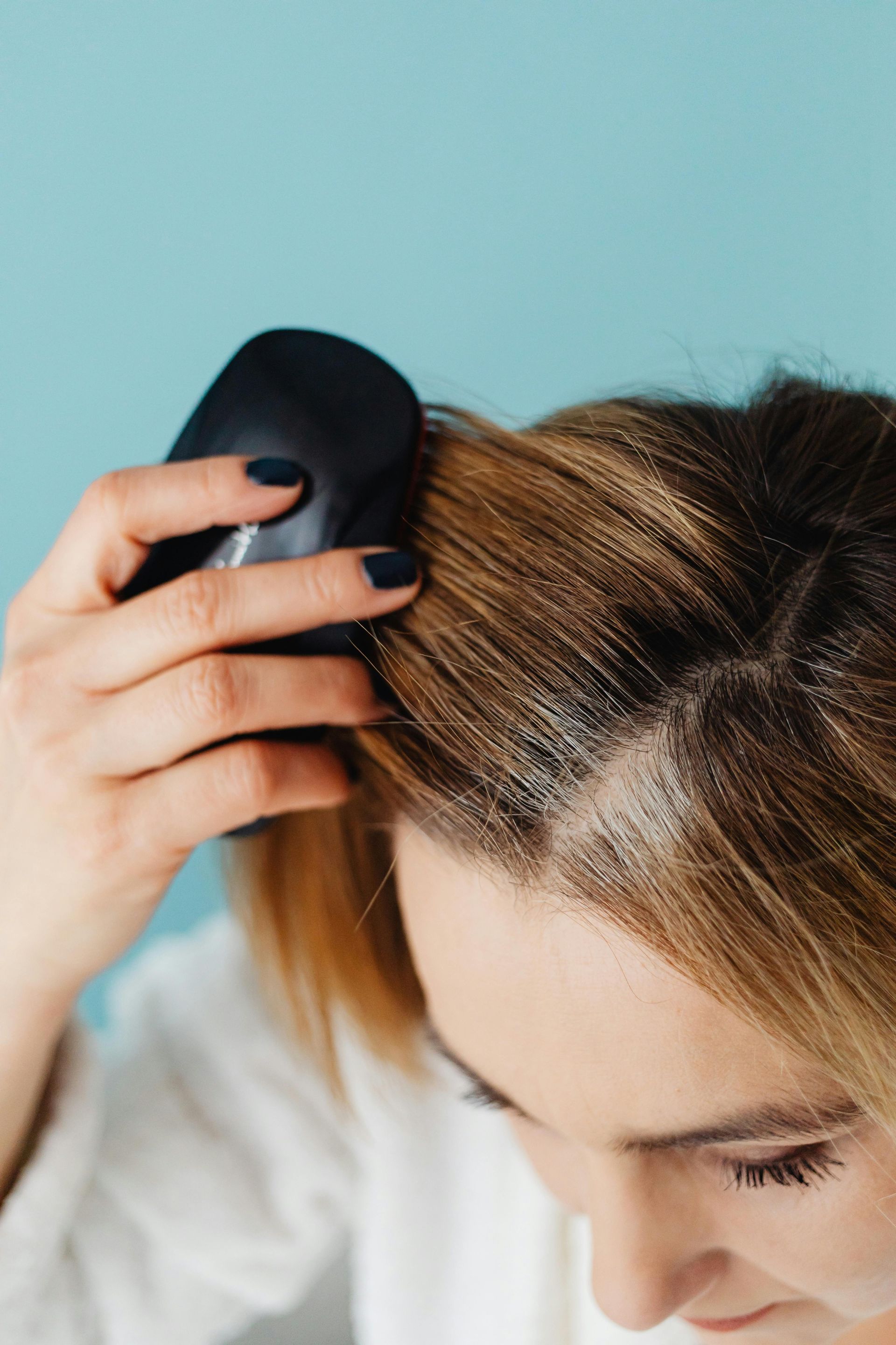 Woman brushing dry shampoo into blonde hair against a blue backdrop.