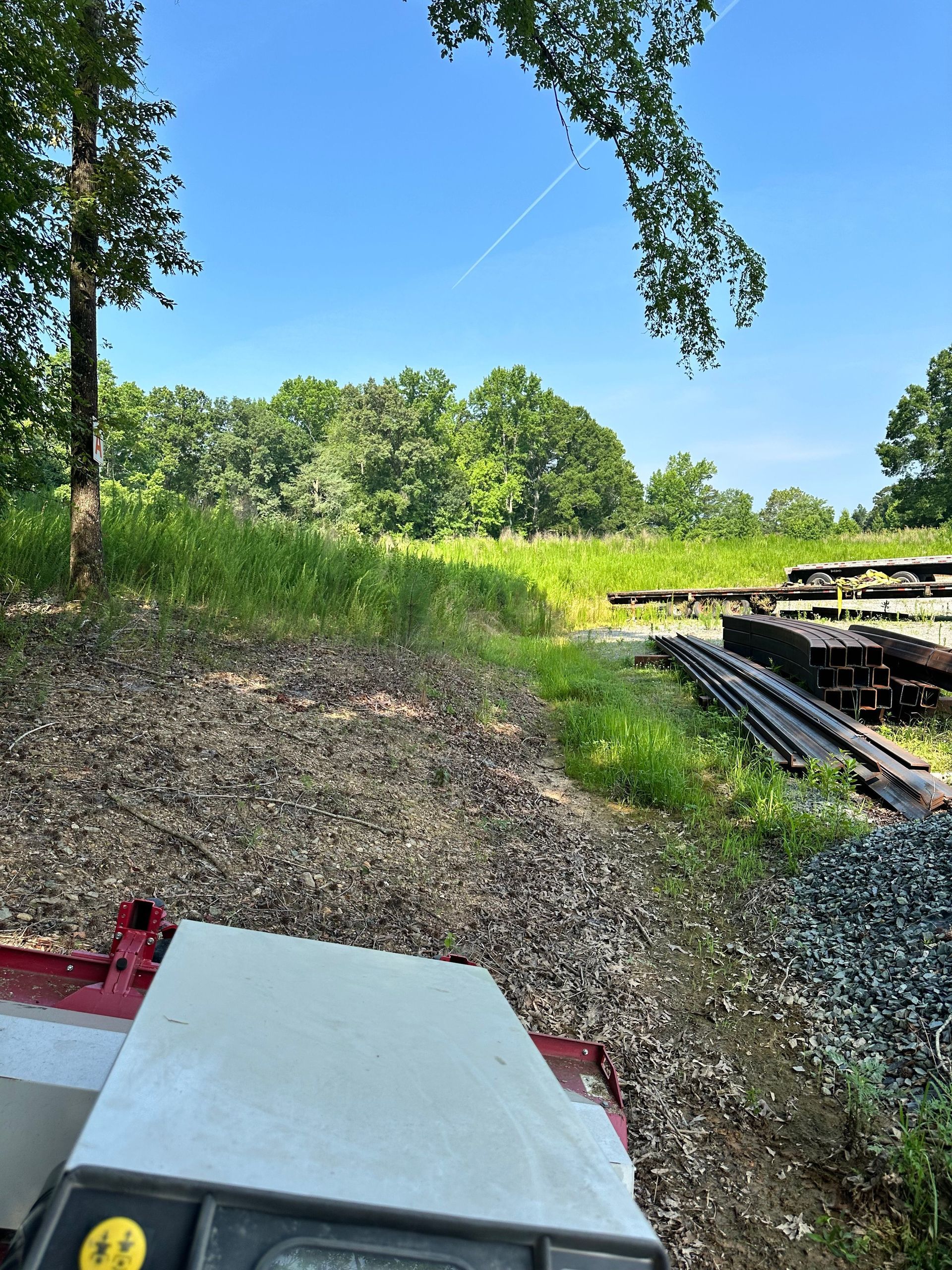 Grassy field with trees and railroad tracks. A sunny day with a blue sky.