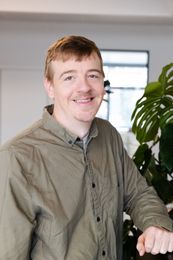 En mand i en grøn skjorte står foran en plante og smiler.